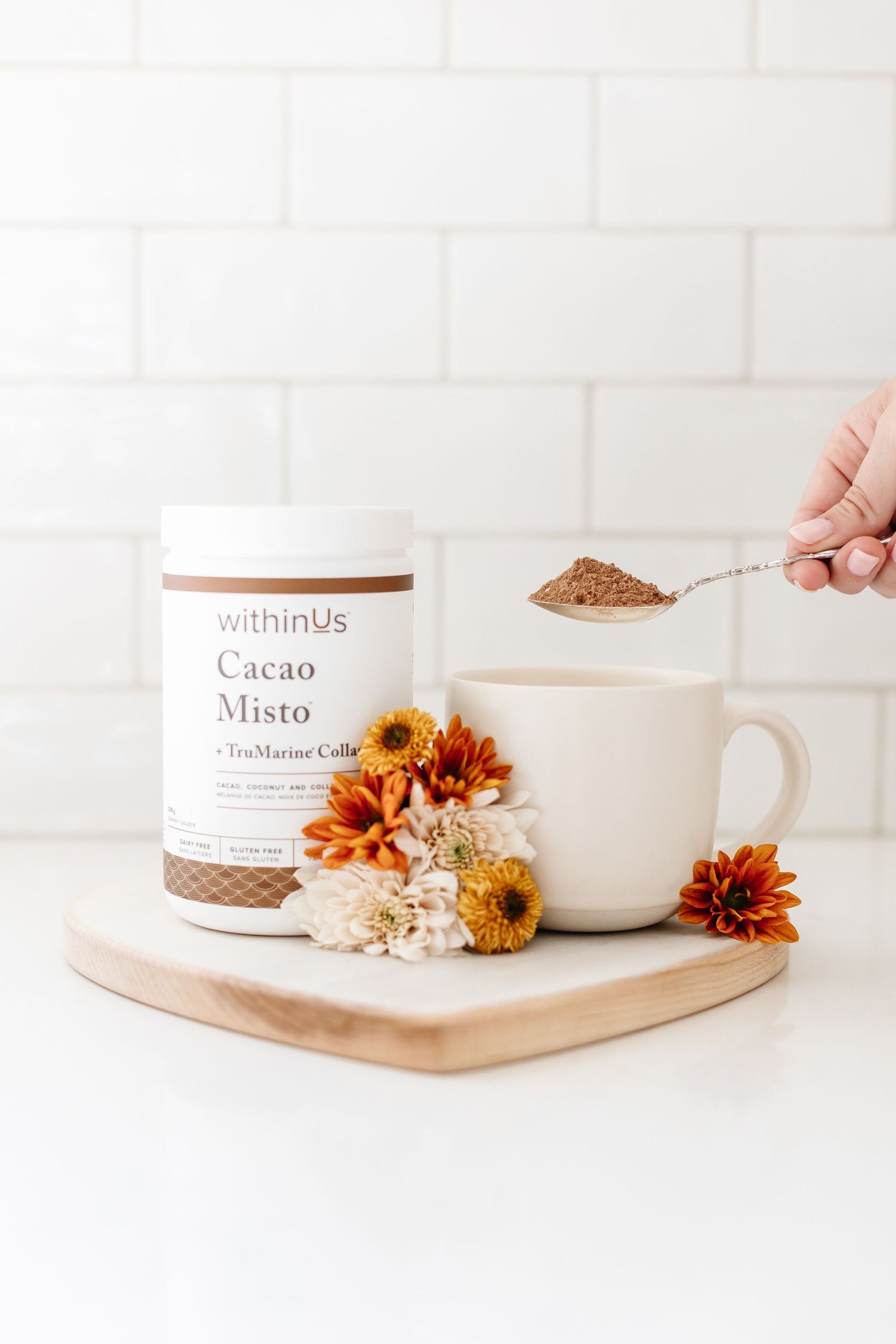White mug and health products displayed with orange flowers on wooden tray for Cacao Misto for WithinUs branding photoshoot in Kelowna BC