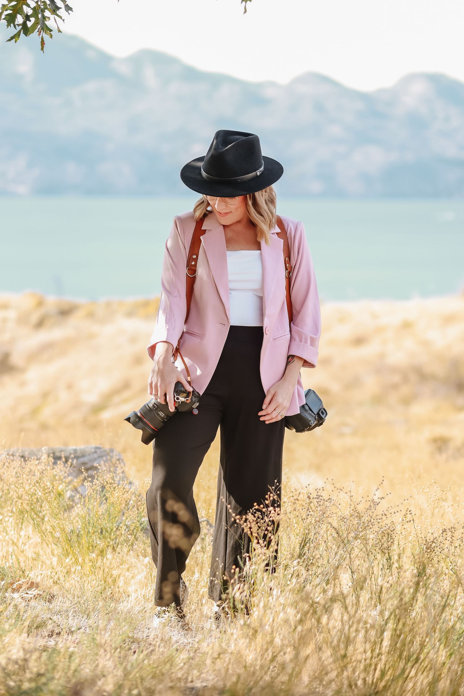 Figure in pink jacket and black hat exploring golden grass field with mountain vista.