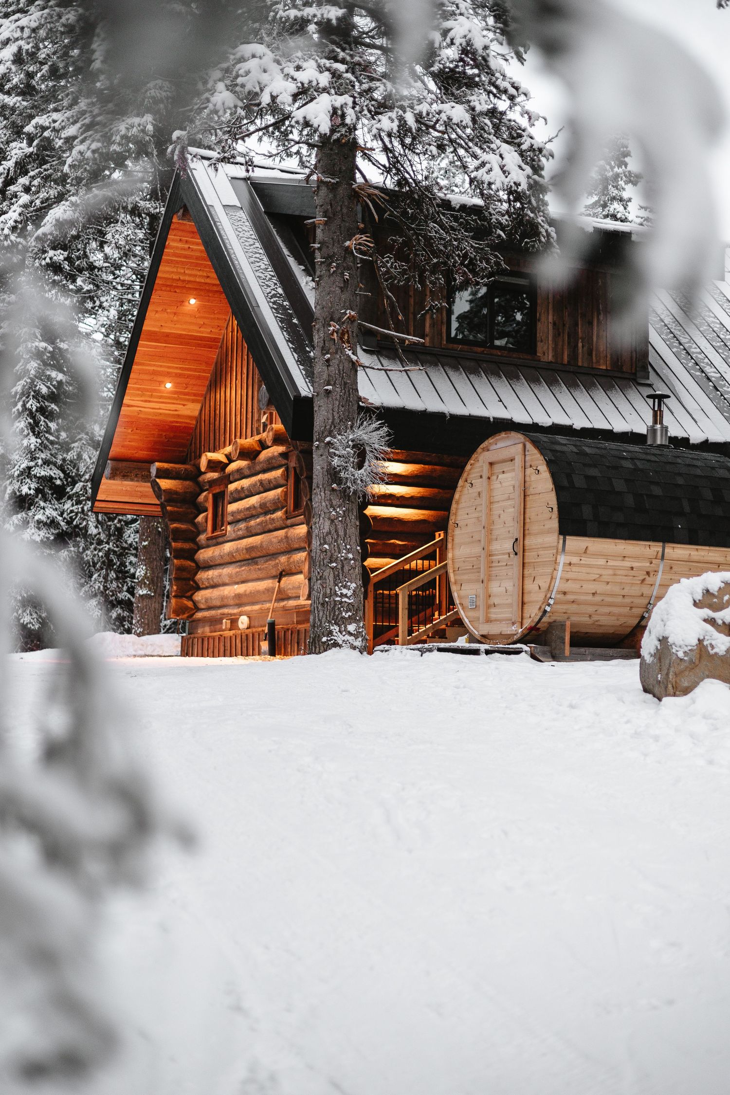 Cozy log cabins nestled in snowy forest with warm glowing windows.