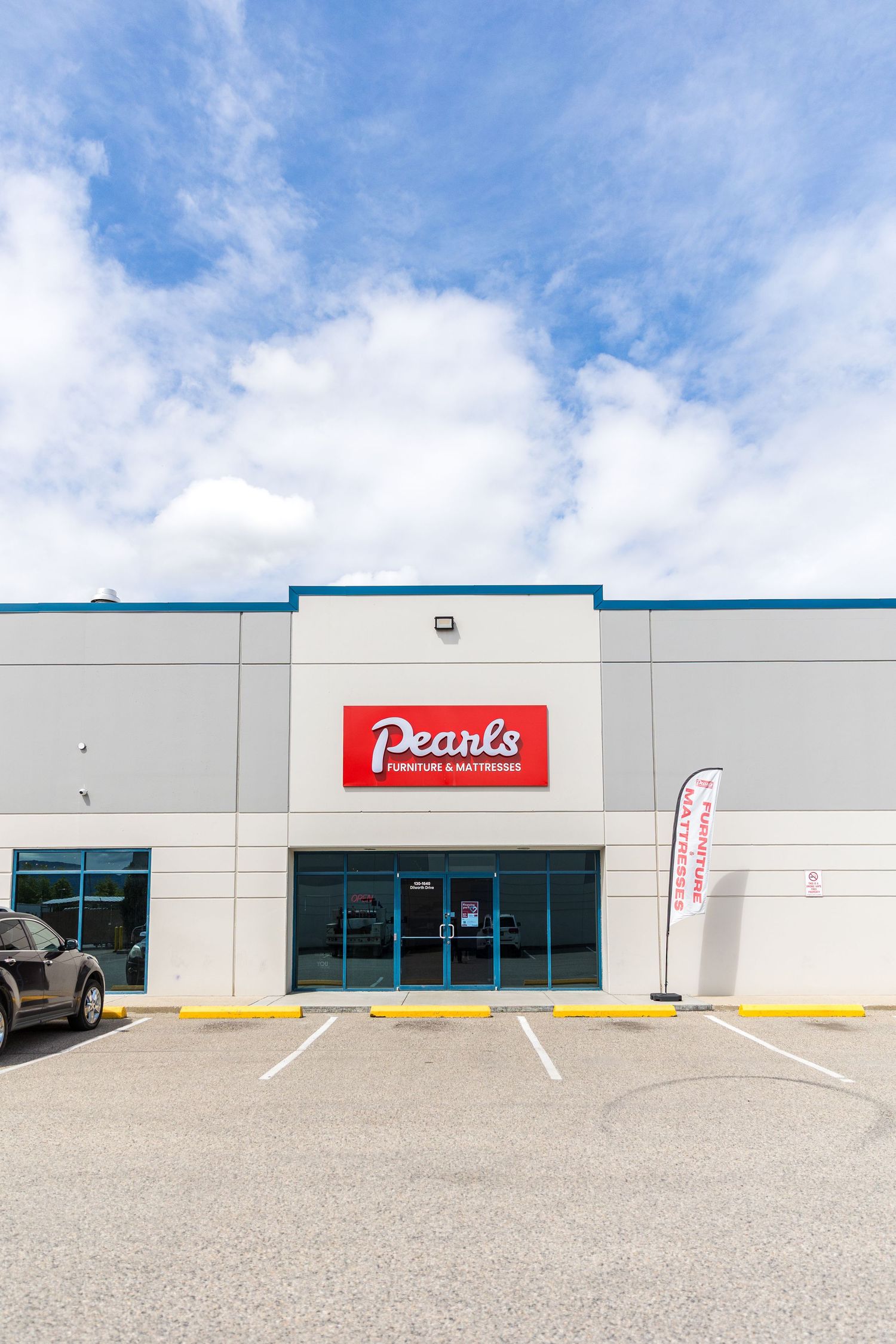 Strip mall exterior with white walls and red signage under blue sky with white clouds.