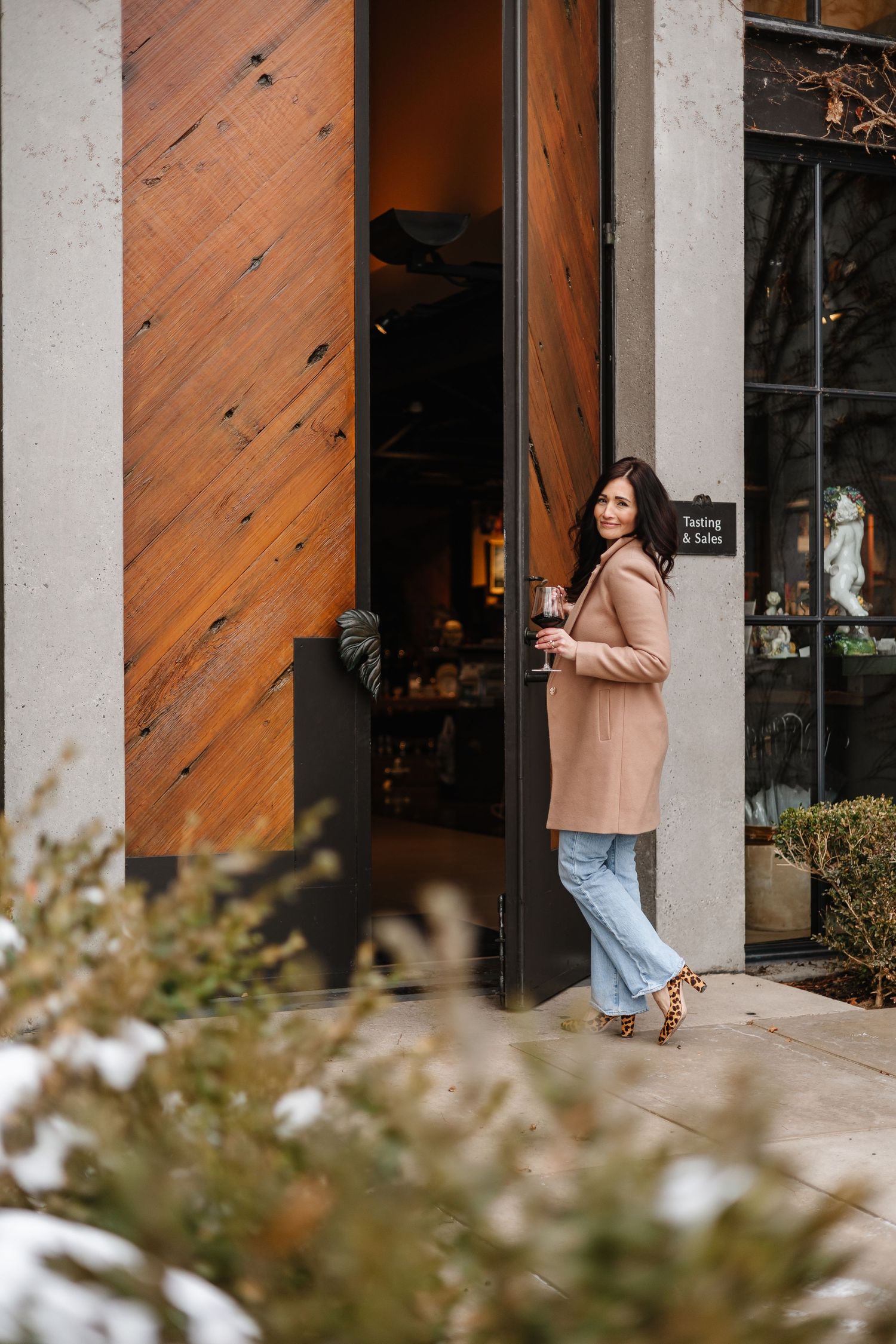 Person in beige sweater and jeans walking through wooden doorway of modern building.