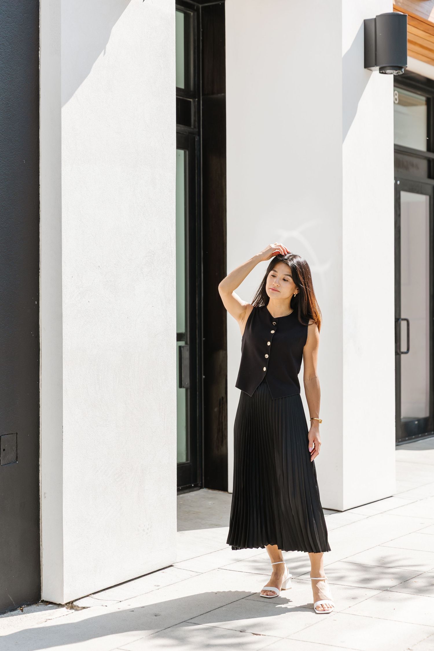 A person in a black sleeveless dress stands between modern white walls and black architectural columns.