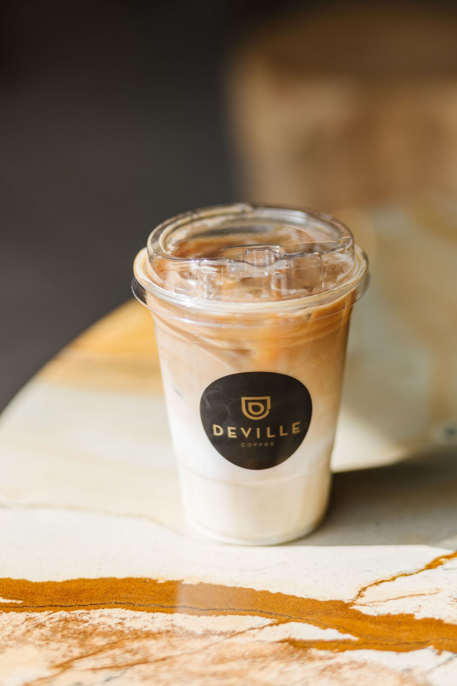 Deville branded coffee cups with creamy foam layered drinks arranged in a row on a rustic wooden surface.