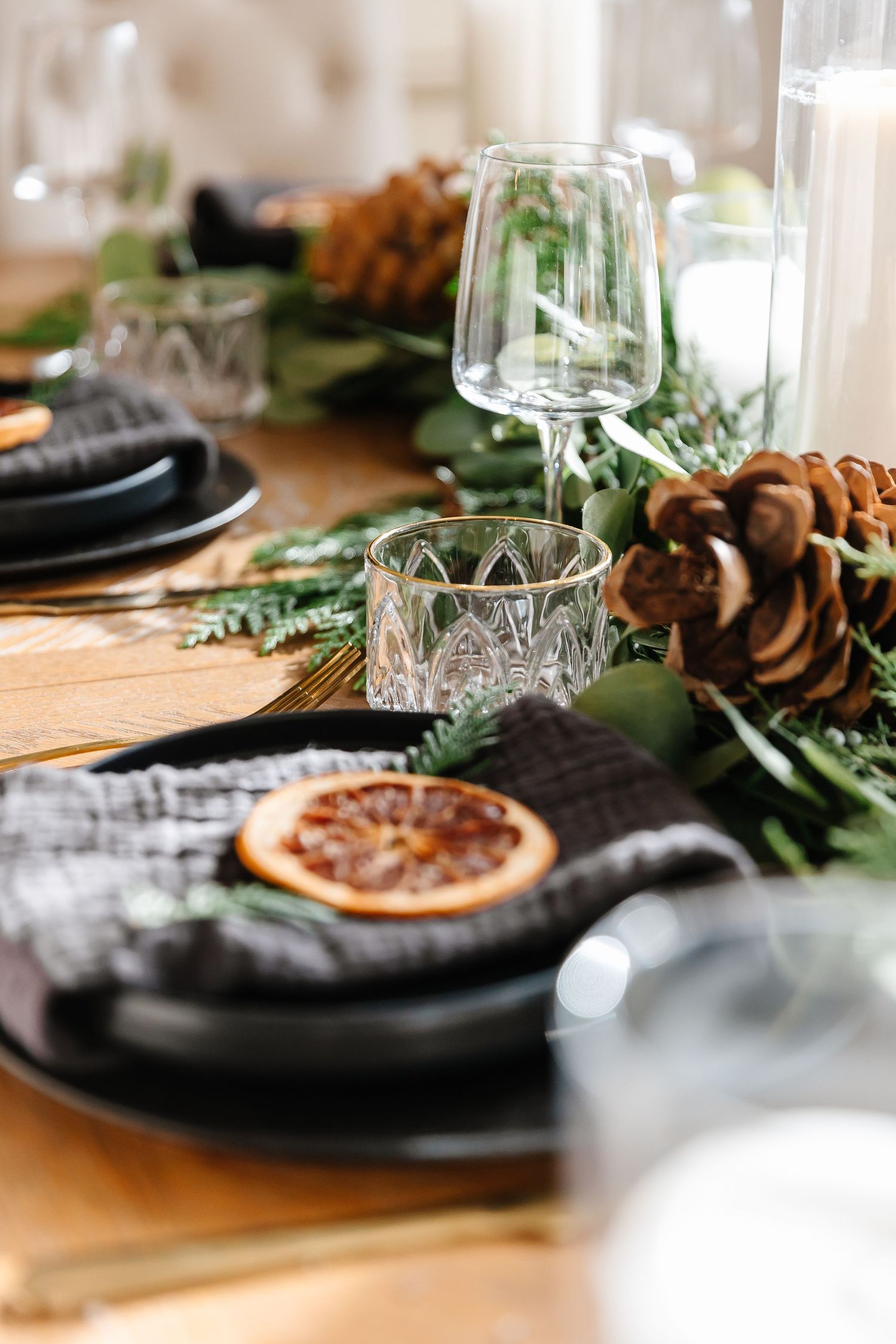 Elegant table setting with black plates, pinecones, and dried orange slices creating a rustic holiday atmosphere.