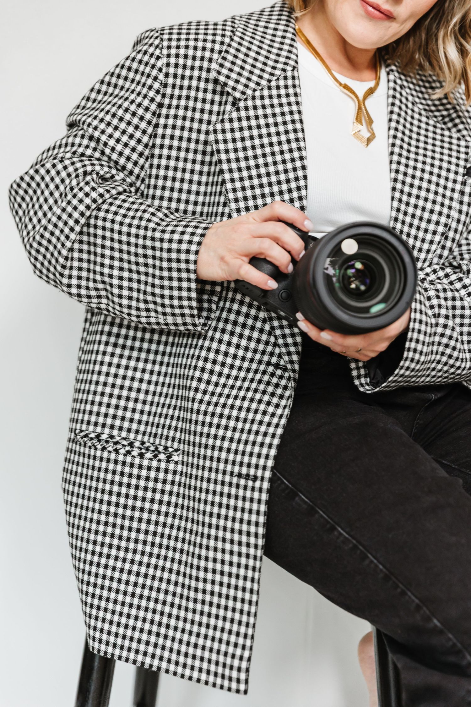 Woman in checkered blazer holding a professional camera, sitting against a white background.