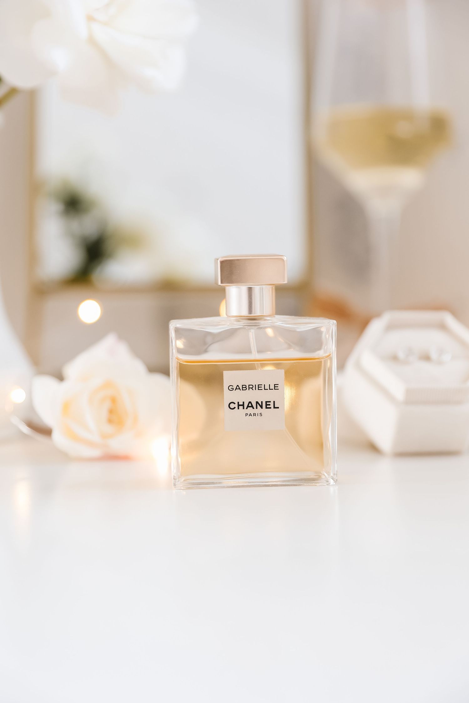 Chanel Gabrielle perfume bottle on white surface with soft pink roses and elegant styling.