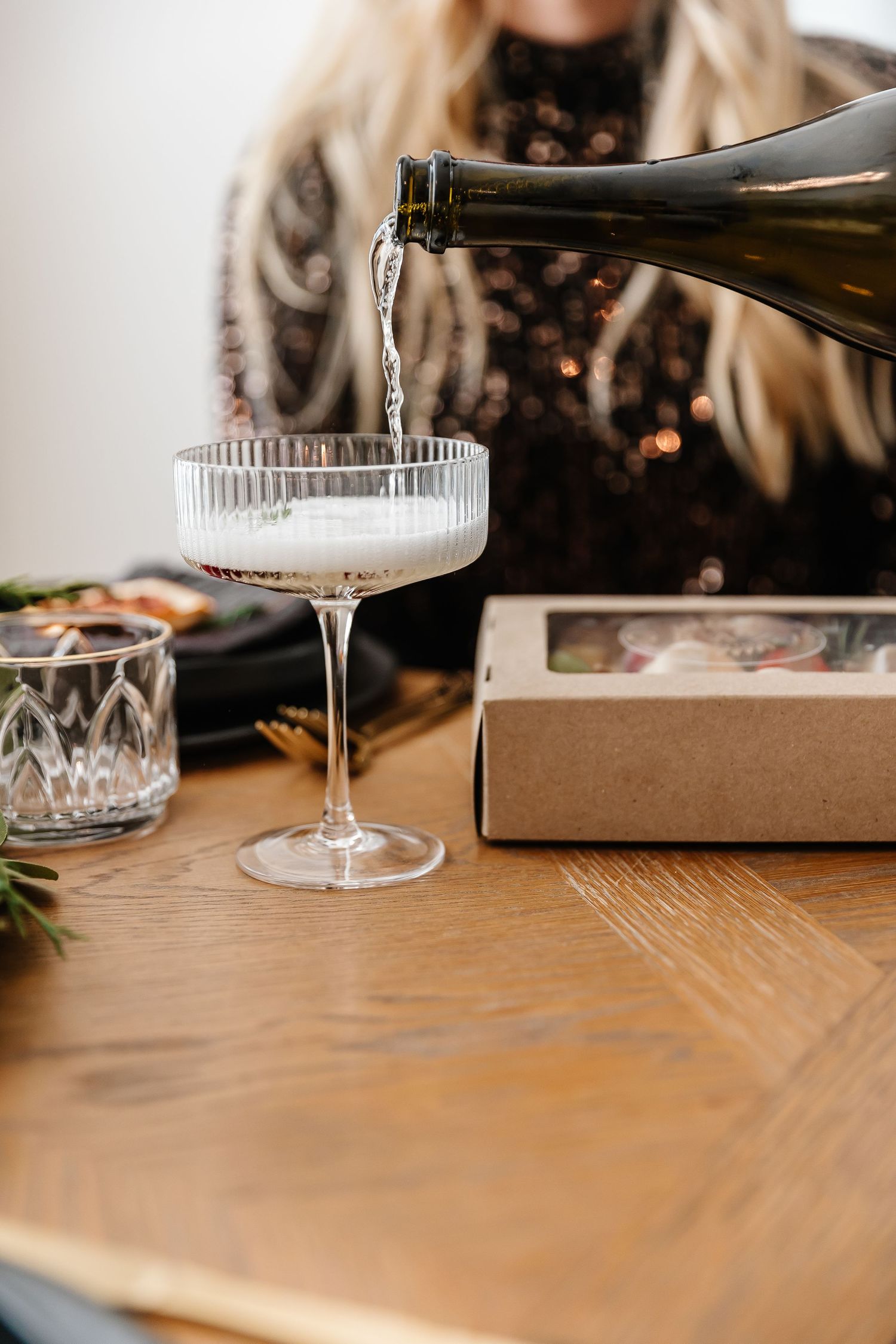 Crystal champagne coupe being filled from a bottle on an elegant wooden dining table.