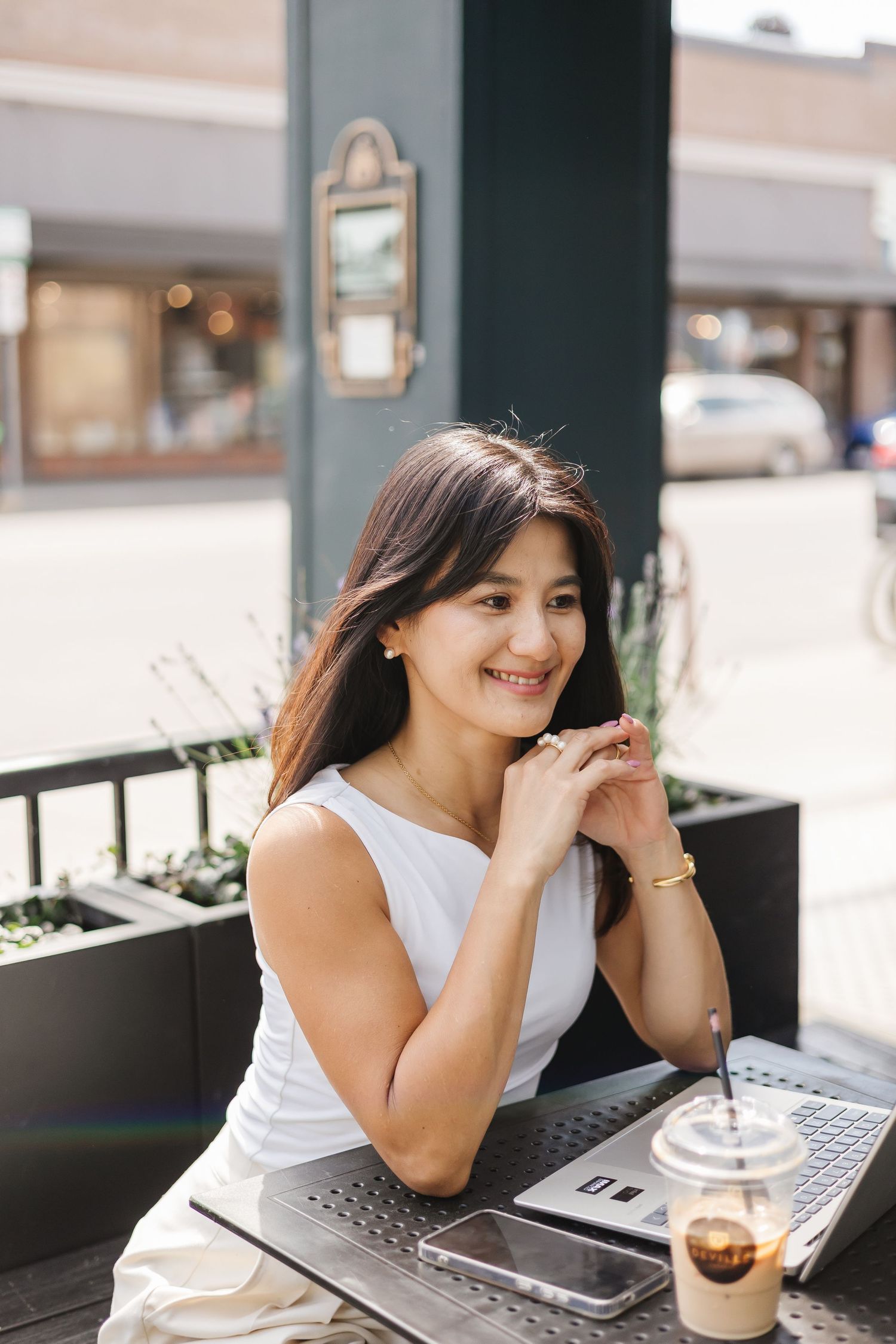 Someone working on a laptop at an outdoor cafe table with an iced coffee drink.