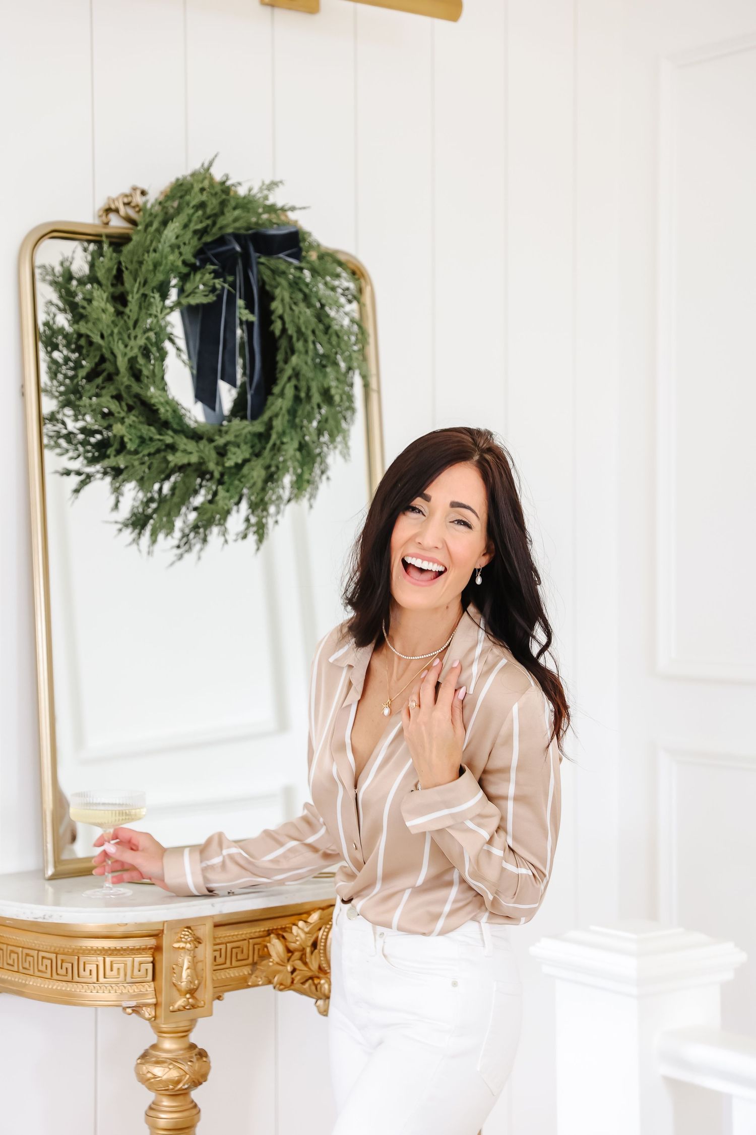 Festive interior scene with gold-framed mirror and evergreen wreath against white wall.