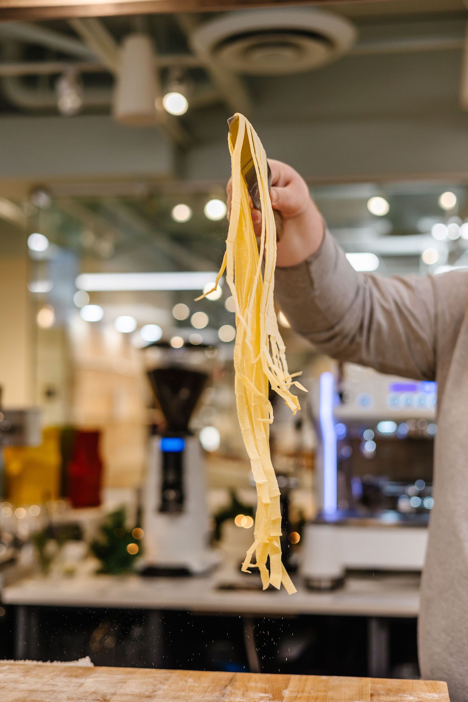 Fresh handmade pasta being lifted in industrial kitchen setting.