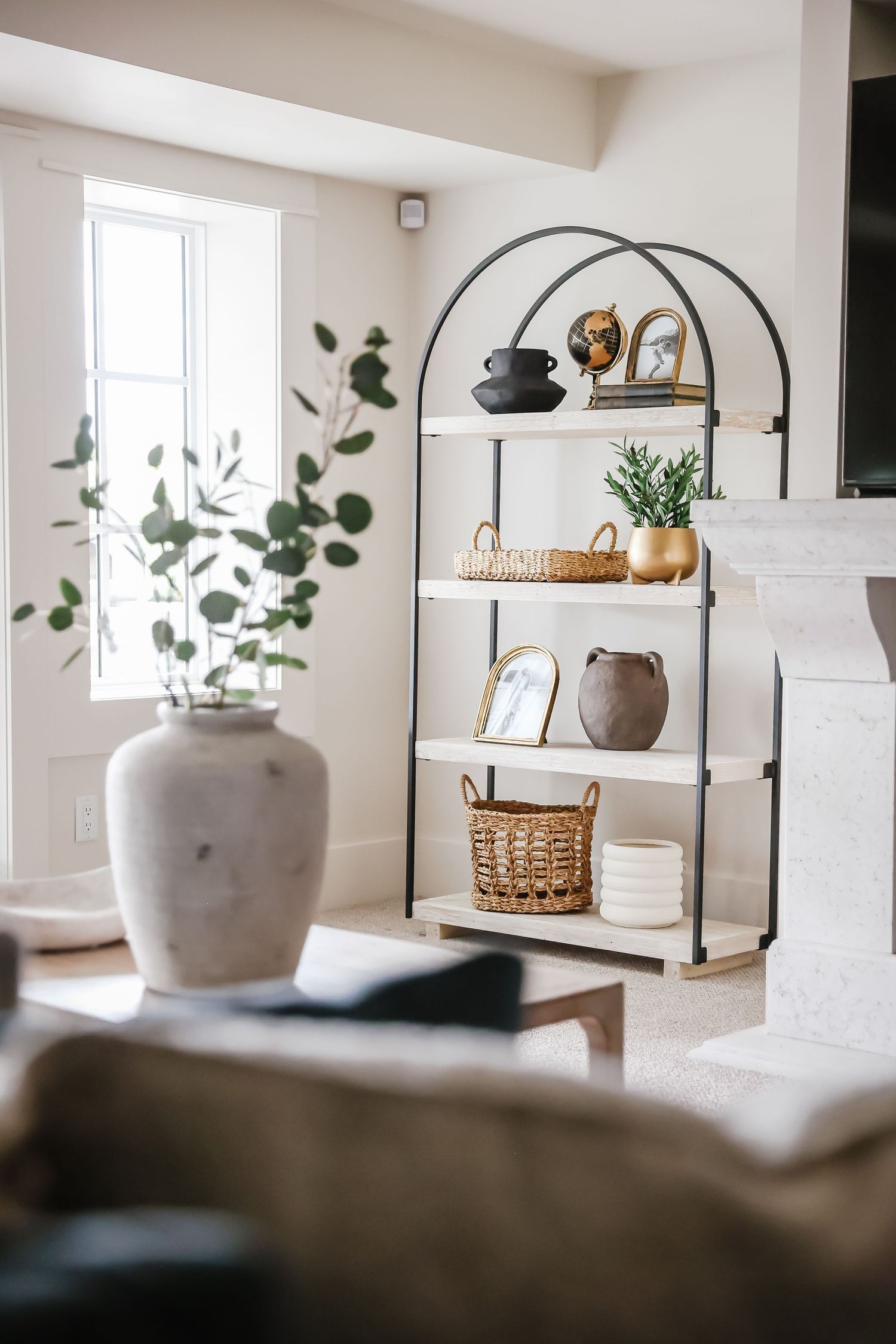Modern white shelf unit with decorative items and plants near bright window.