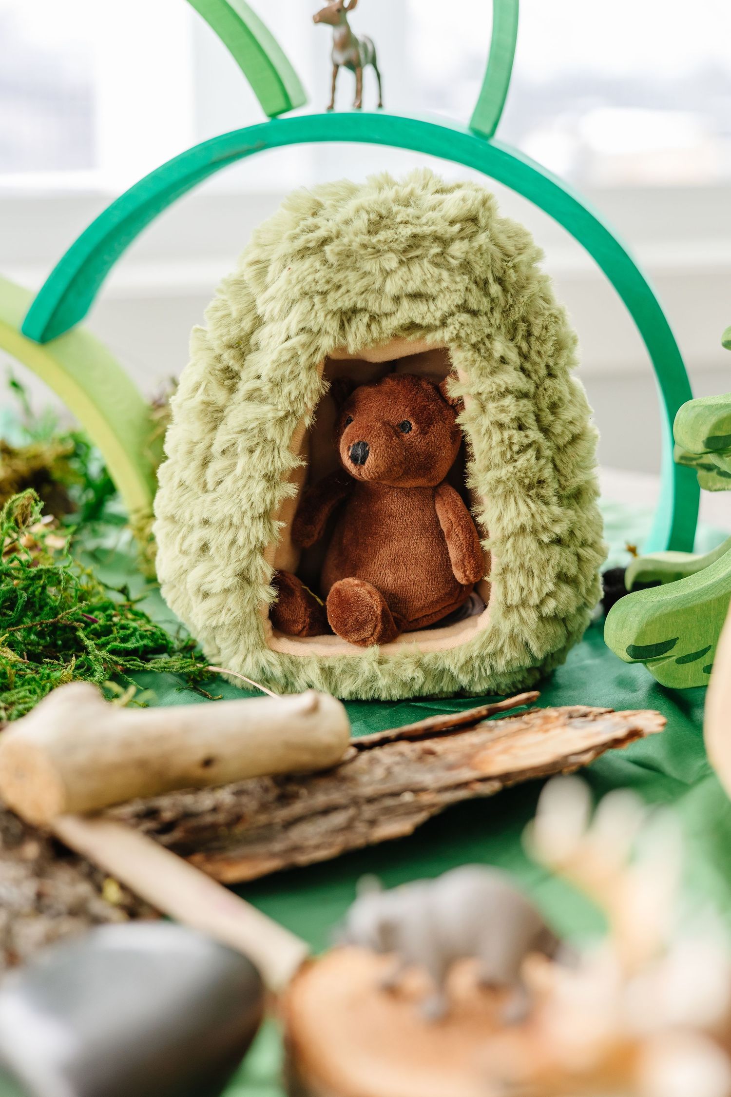 Small brown plush toy bear sitting inside a cozy green nest-like structure.