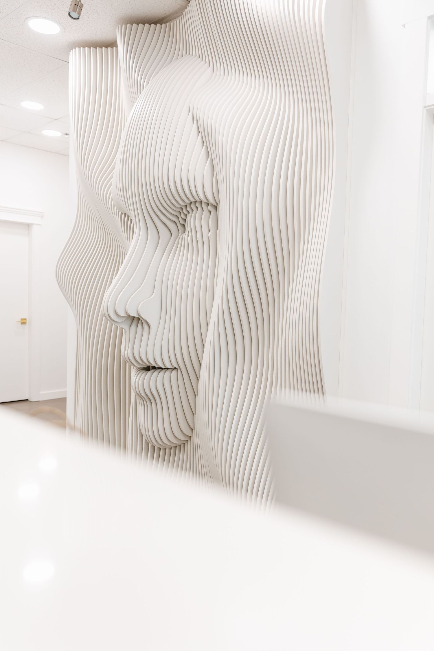 Abstract white wavy wall installation with curved geometric patterns creates a flowing sculptural effect in gallery space.