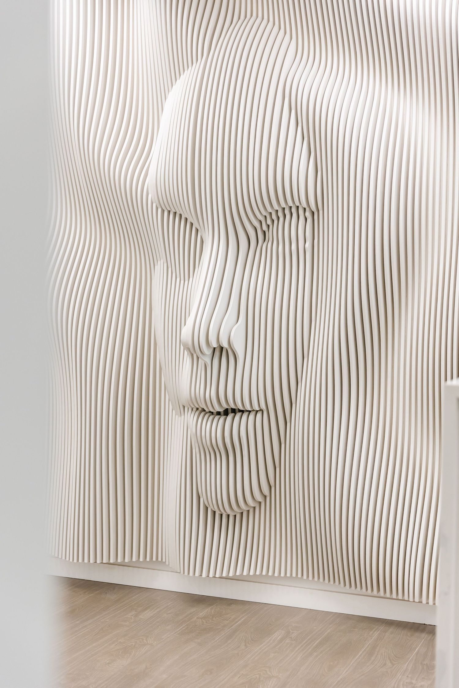 Abstract white sculptural wall installation with undulating vertical lines creates a mesmerizing ripple effect pattern.