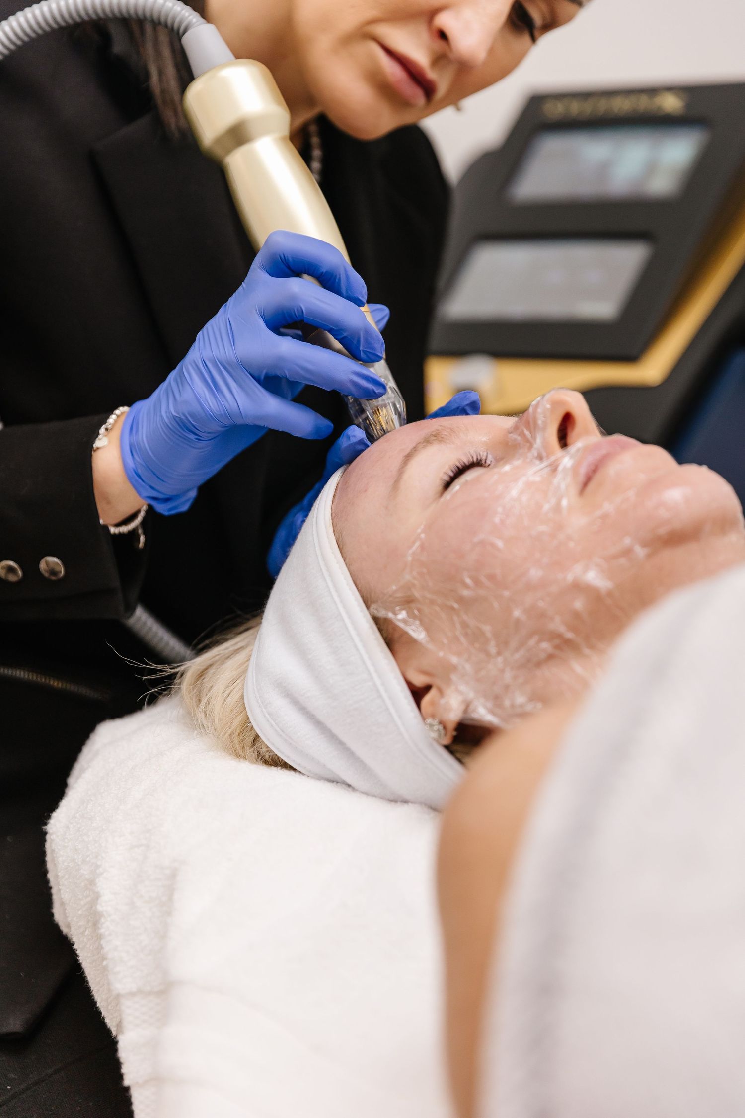 Professional cosmetologist performs facial treatment with white cream mask and blue protective gloves.