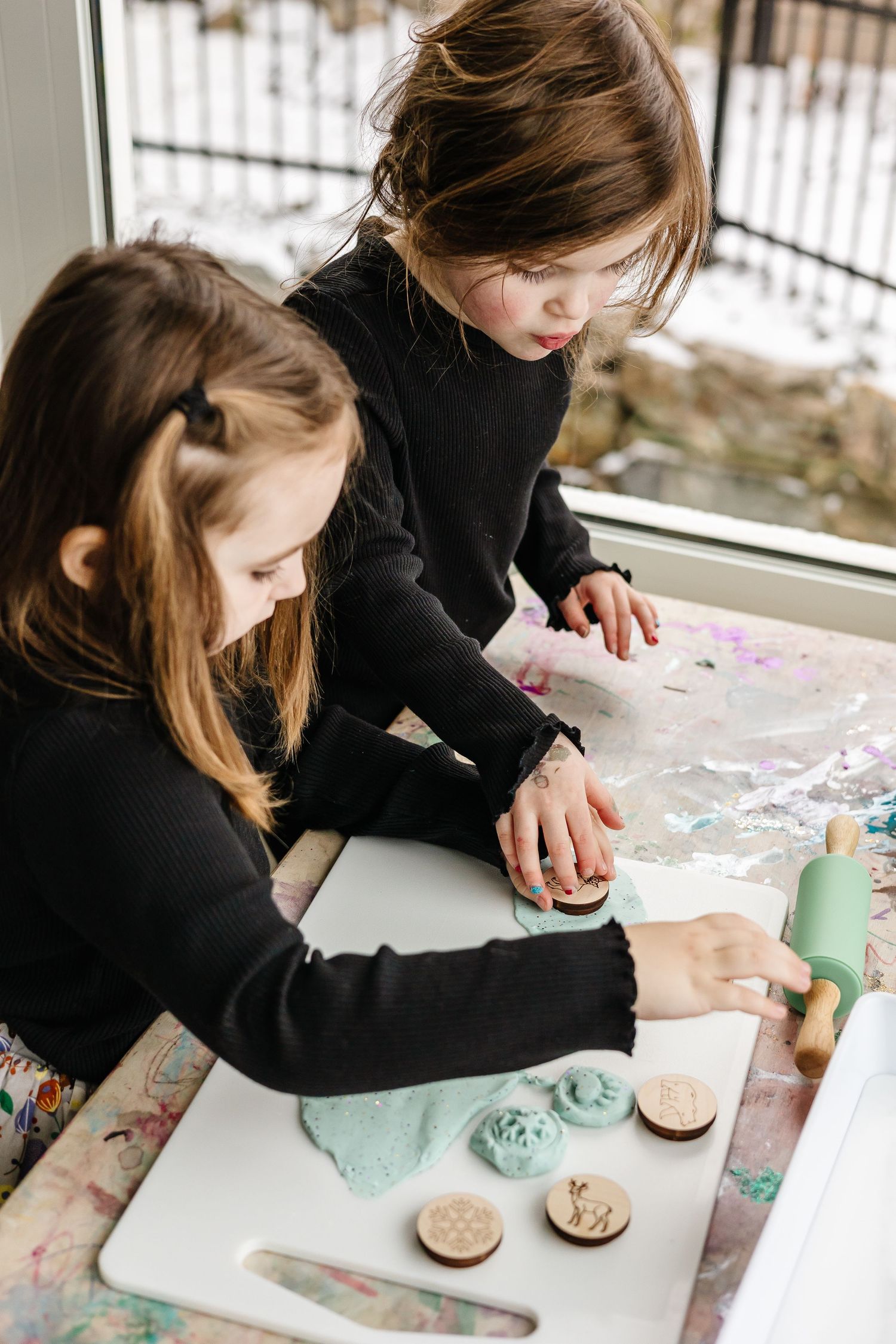 Hands working with crafting materials and stamps on a white surface.