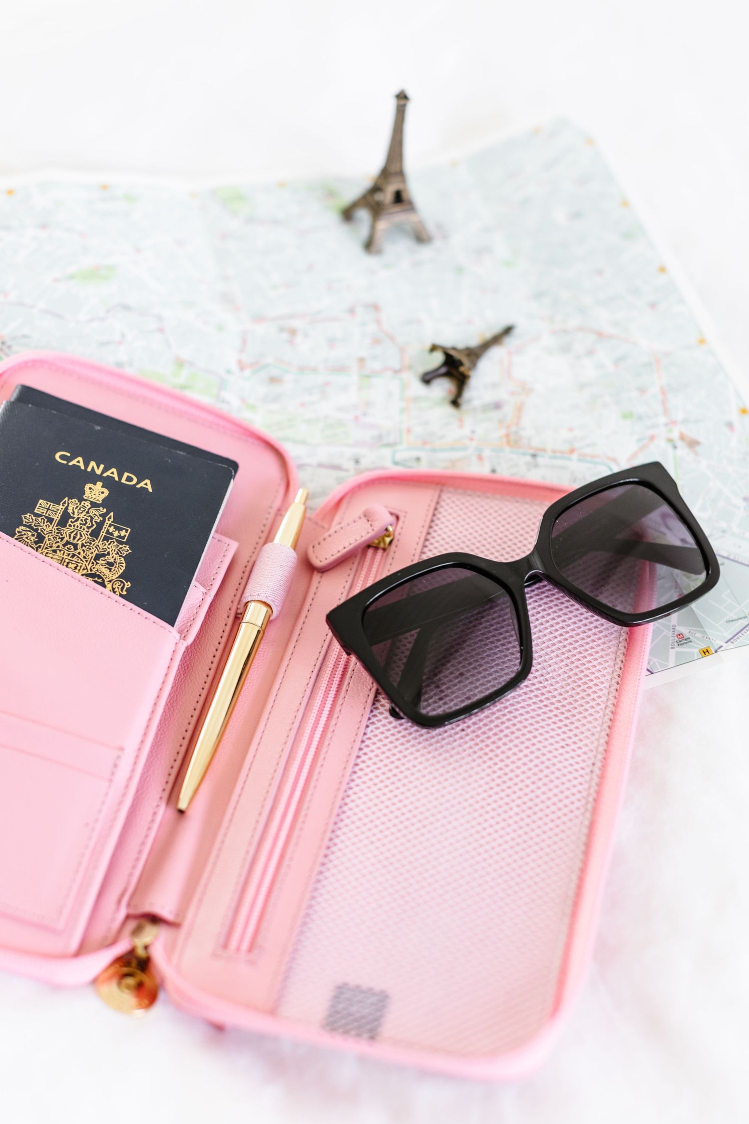 Pink passport holder with sunglasses and pen displayed on a map background.