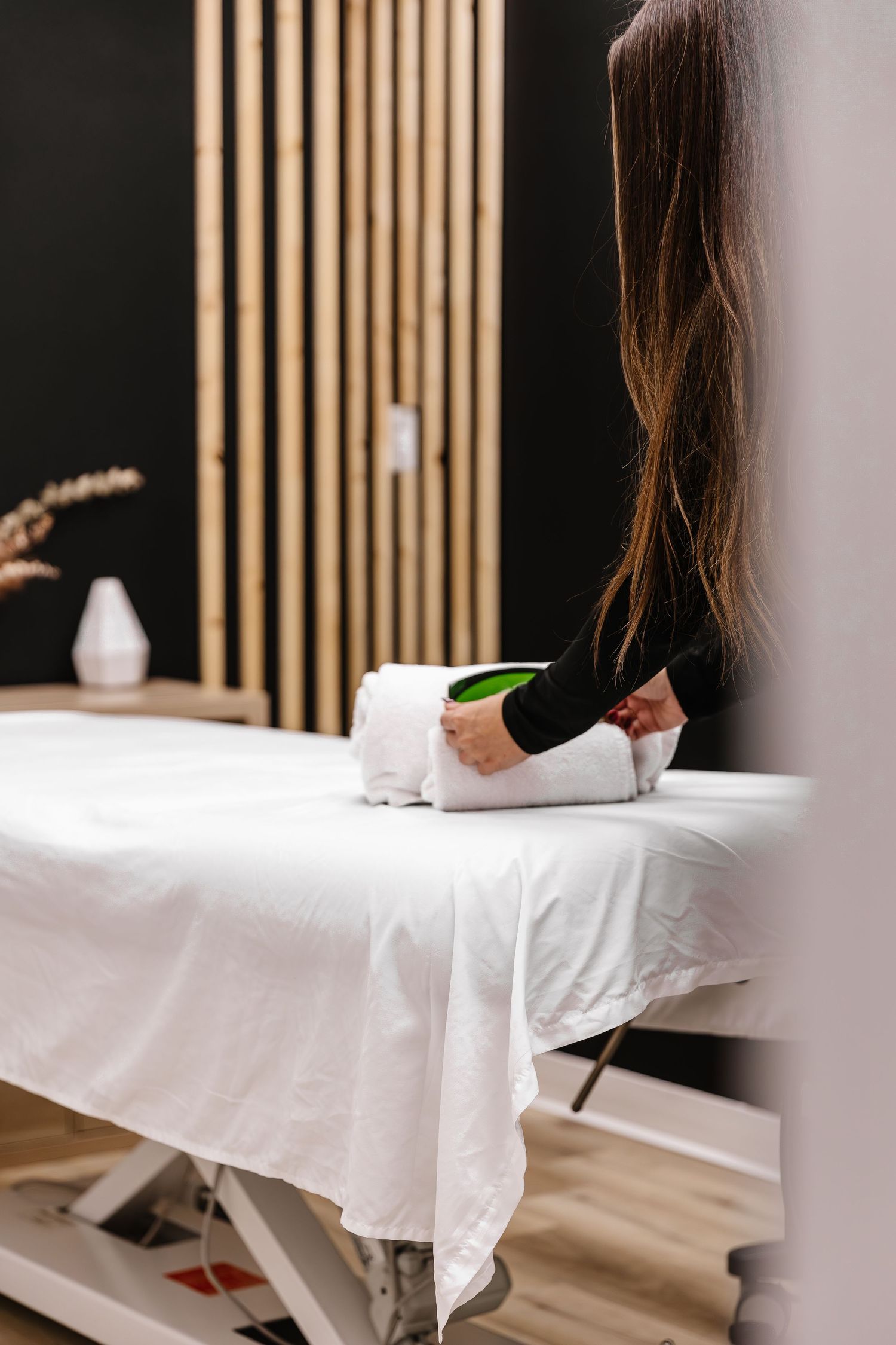 Clean spa treatment room with white massage table and wooden slat wall divider.