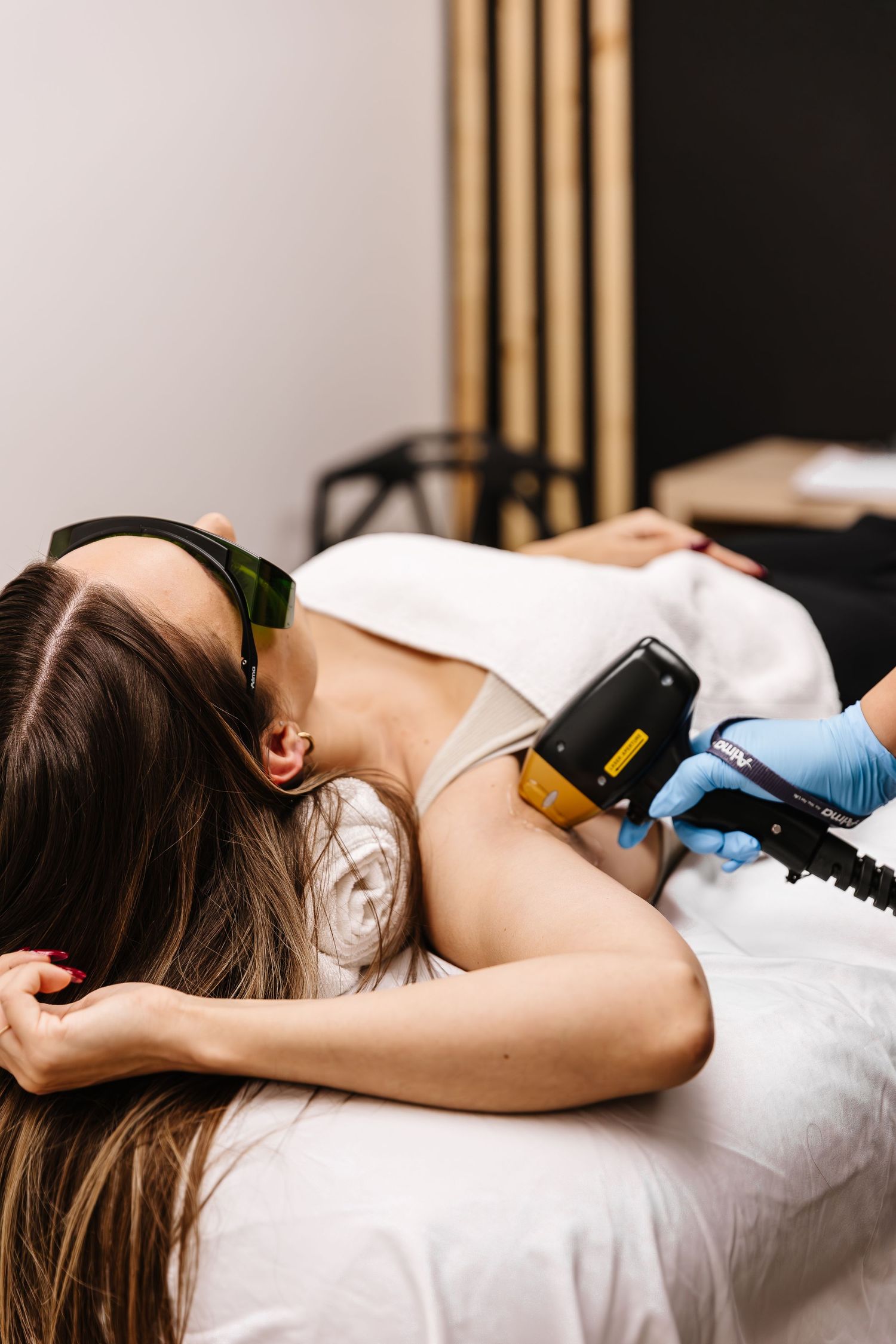 Woman lying on massage table receiving laser hair removal treatment at a beauty spa.