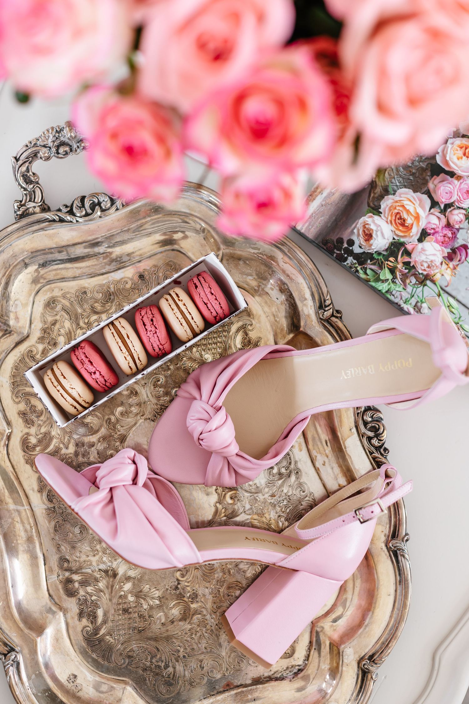 Pink macarons and bow heels arranged on vintage silver tray with pink roses.