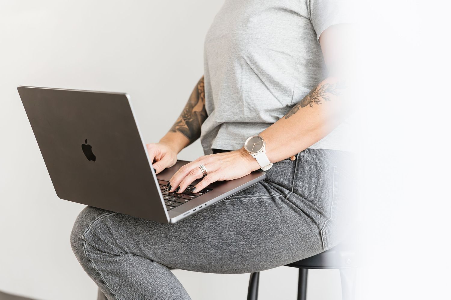 Person working on laptop while sitting at desk with grey sweater and white shirt visible in professional setting.