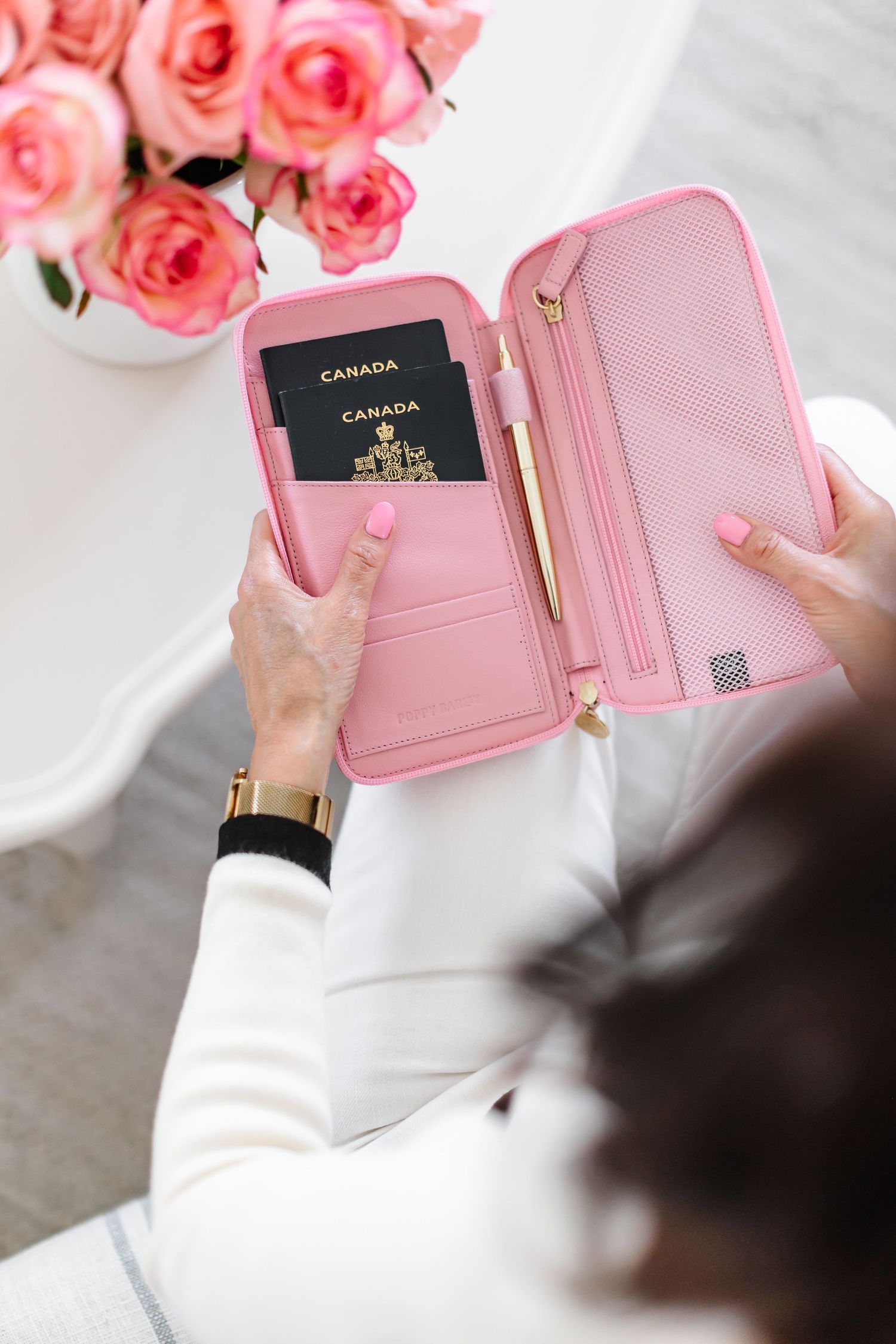 Hands holding pink passport wallet with Canadian passport visible.