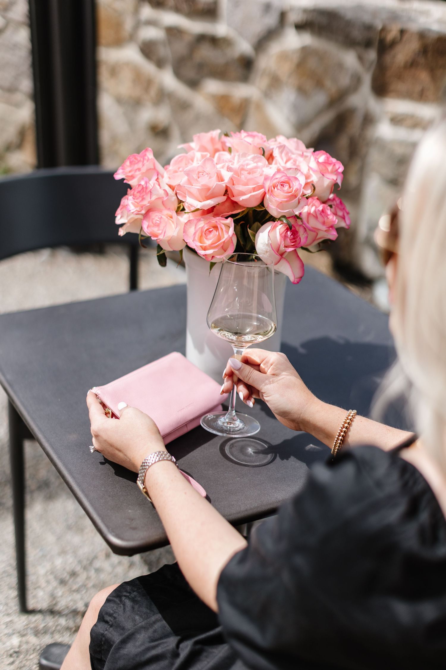 Pink roses in glass vase next to hands holding pink wallet on dark surface.