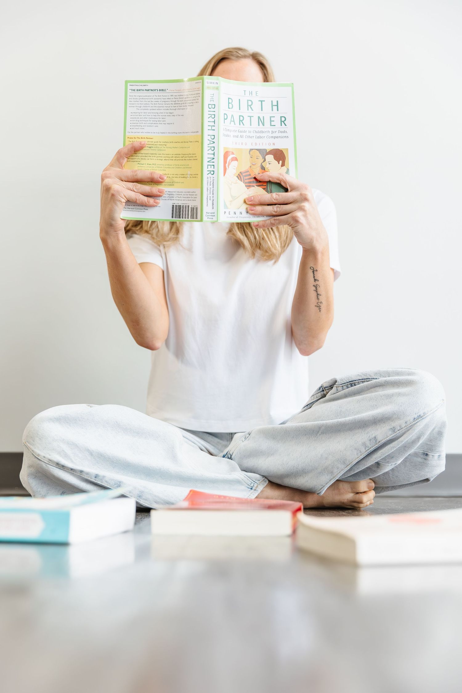Someone in casual white shirt and gray pants sits cross-legged on floor reading a book.