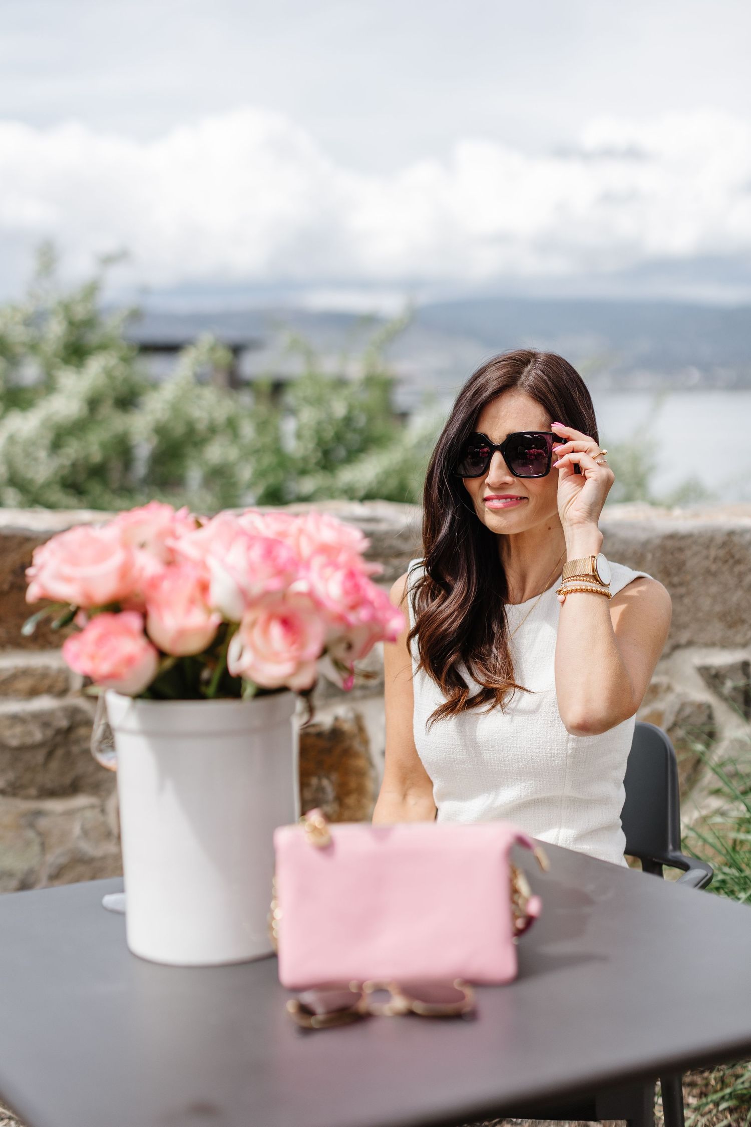 Outdoor scene with pink roses and travel accessories on stone patio table.