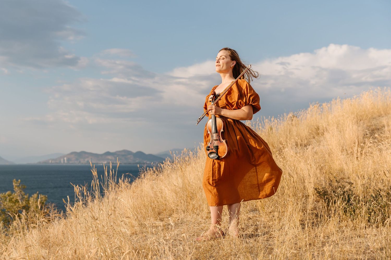 Person in flowing dress twirling on hilltop against golden sunset landscape.
