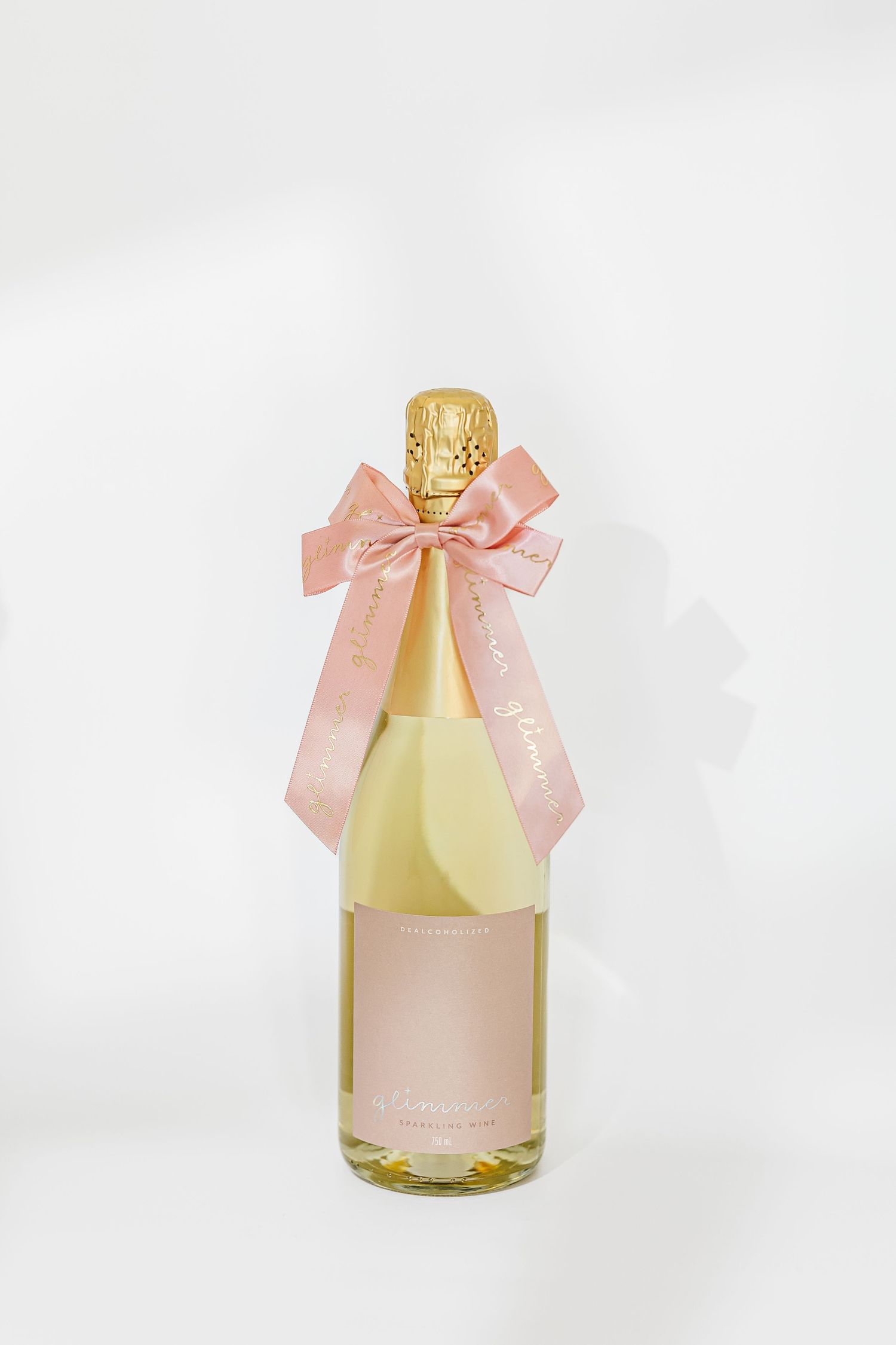 Small pink champagne bottles with blush ribbon bows and gold caps displayed at different angles on white background.