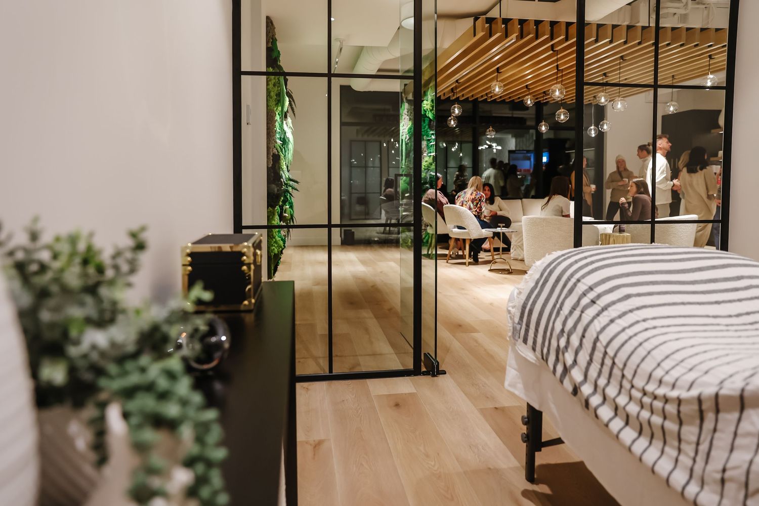 Modern bedroom interior with glass doors, wooden floors, and green plants creating a contemporary living space.
