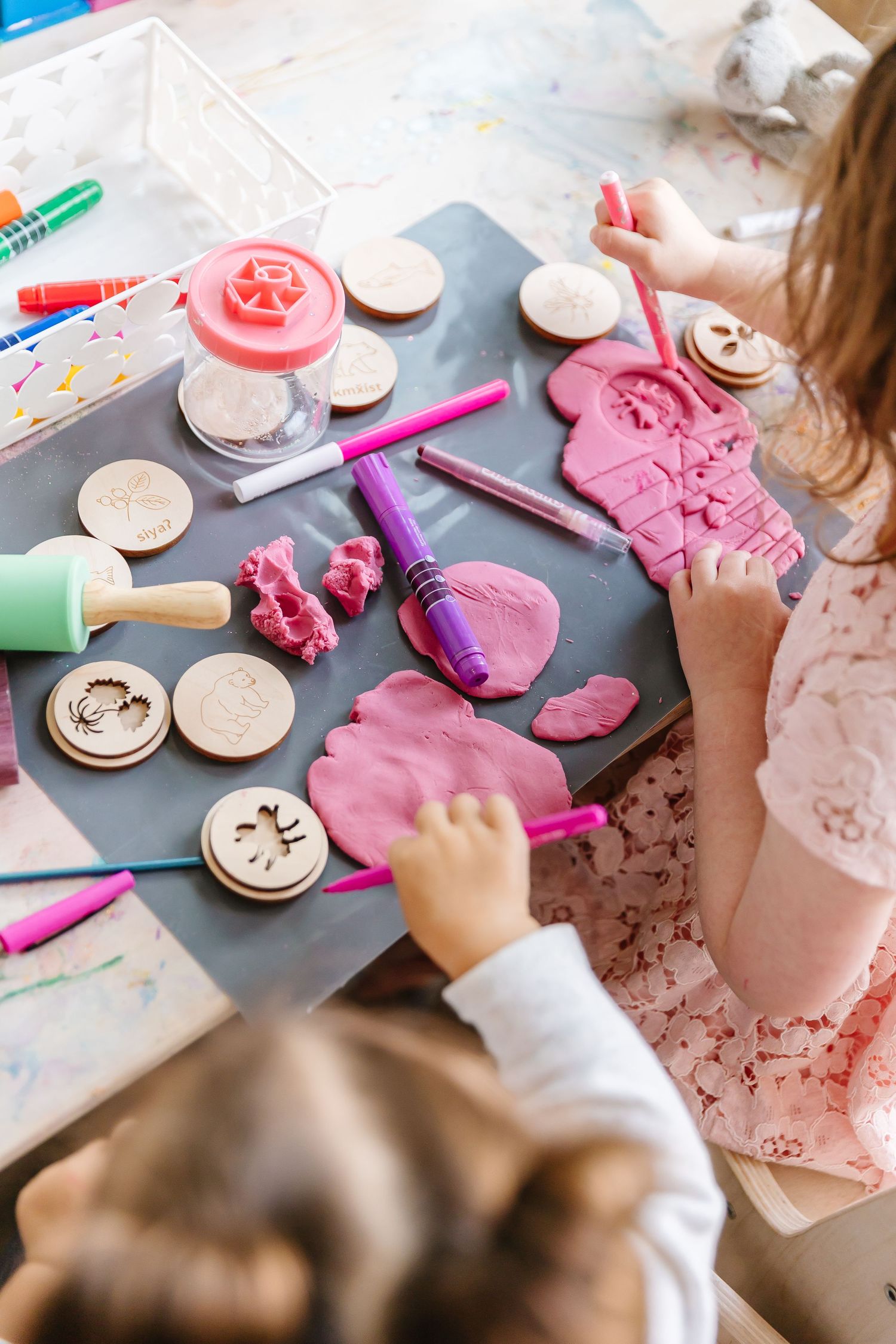 Close-up view of hands working with pink play dough and cookie cutters on a dark surface.