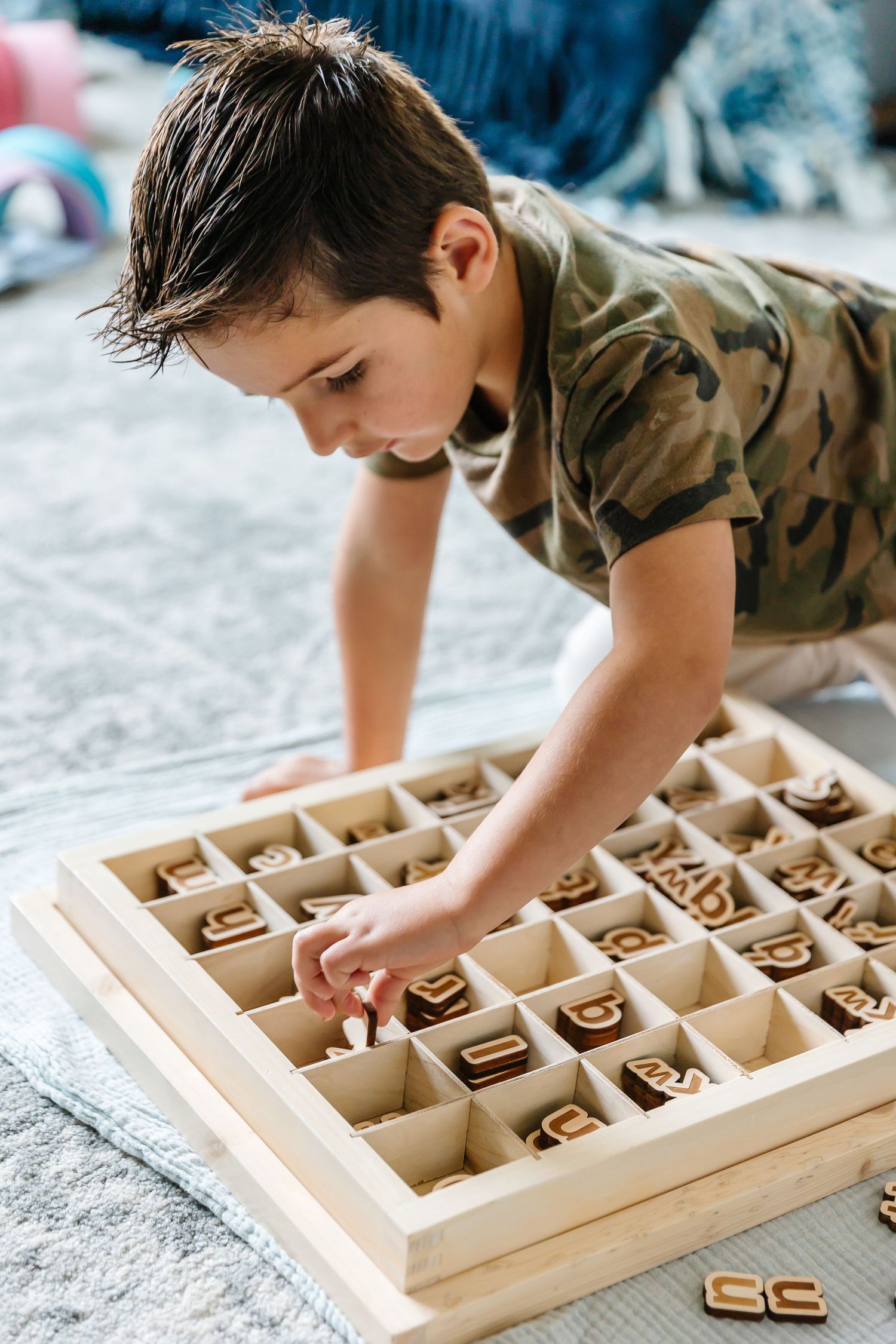 Child playing with a wooden alphabet sorting board on a carpeted floor.