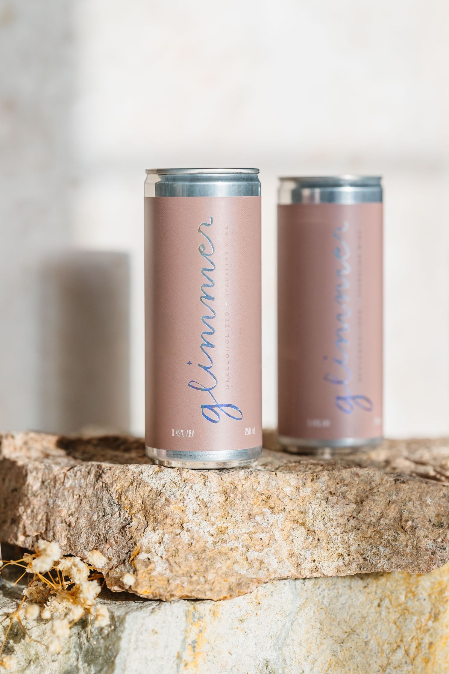 Pink metallic beverage cans arranged on a textured stone surface with soft lighting and shallow depth of field.