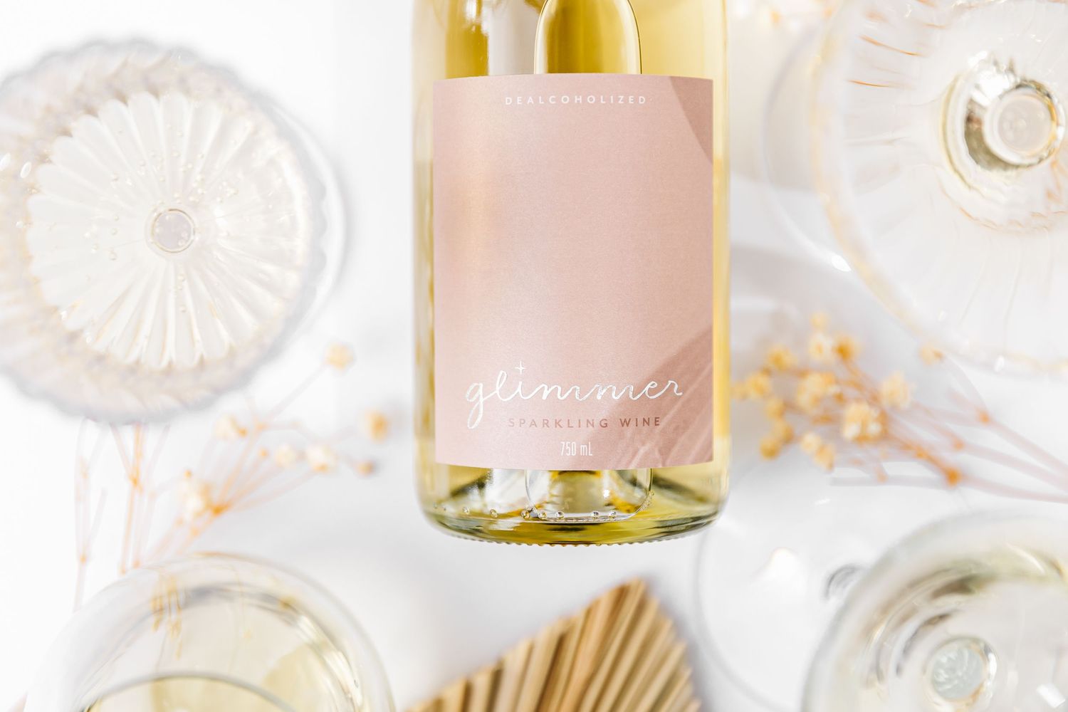 Elegant table setting with white decorative plates, gold accents, and a bottle of white wine against a light background.