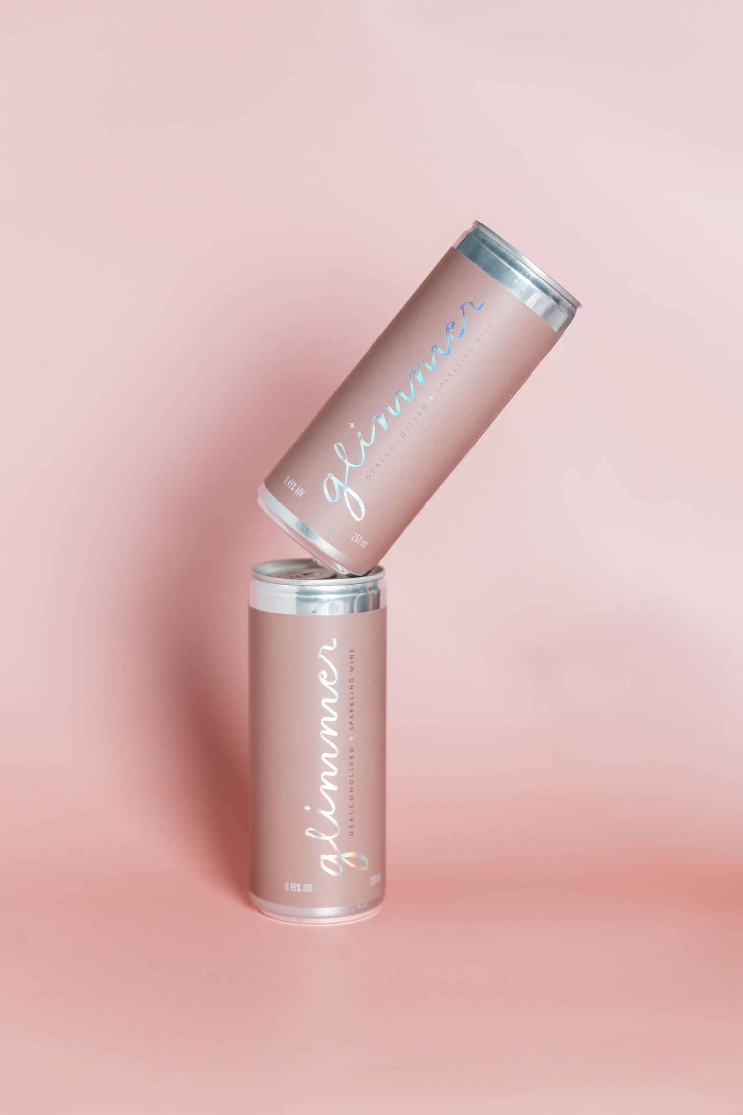 Two pink metallic beverage cans balanced at an angle against each other on a pink background.