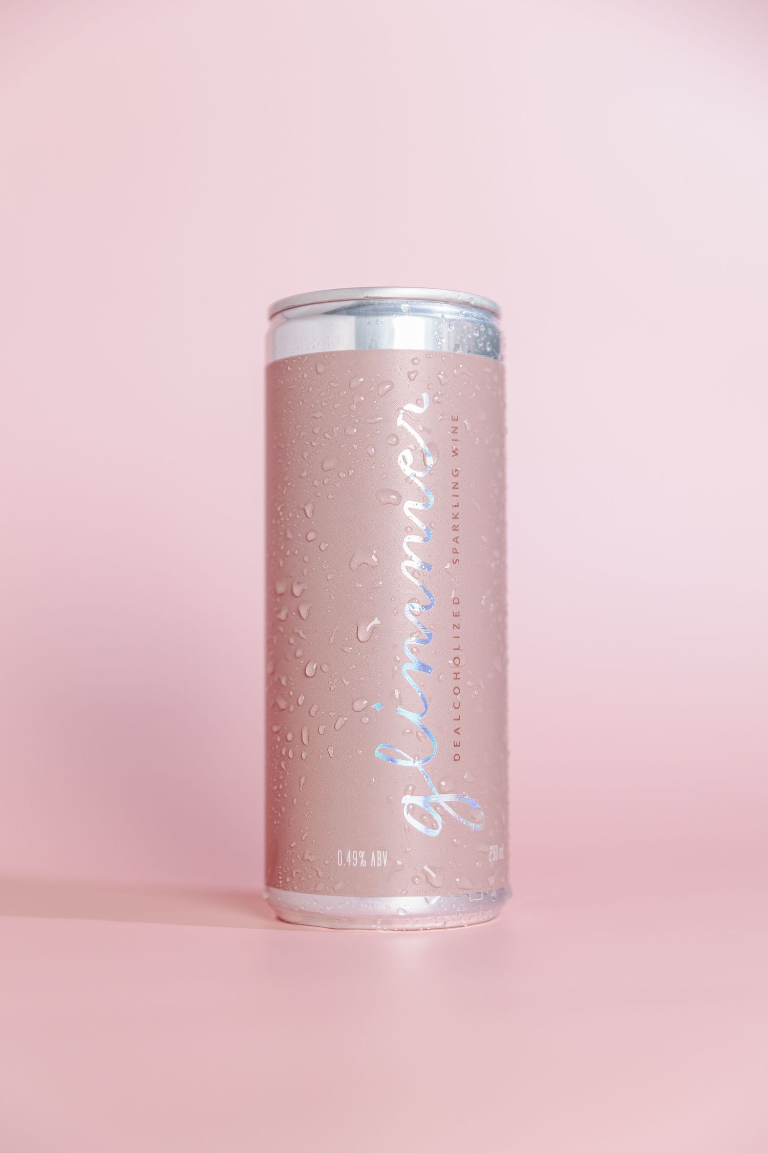 Pink and silver cylindrical beverage can with water droplets against soft pink background shown from multiple angles.
