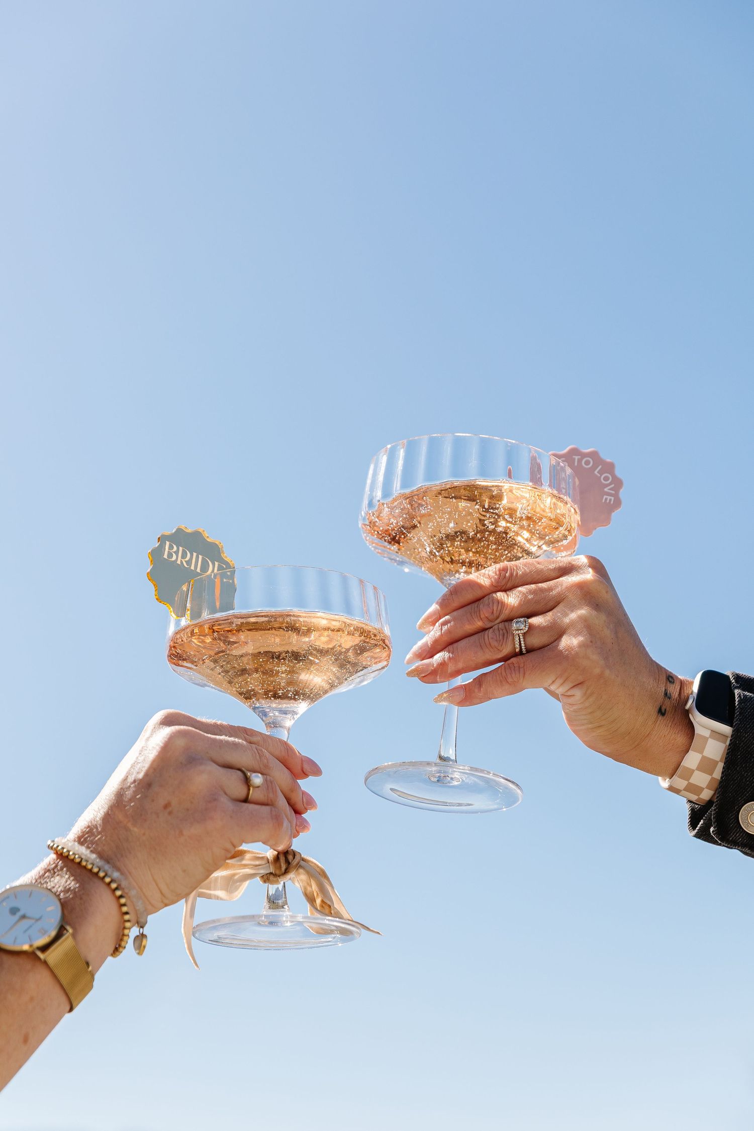 Three hands toasting with champagne glasses against a bright blue sky background.