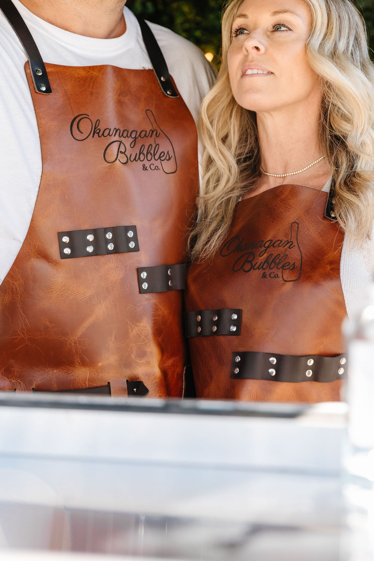 Brown leather aprons with metal studs and branding details shown in close-up product photography.
