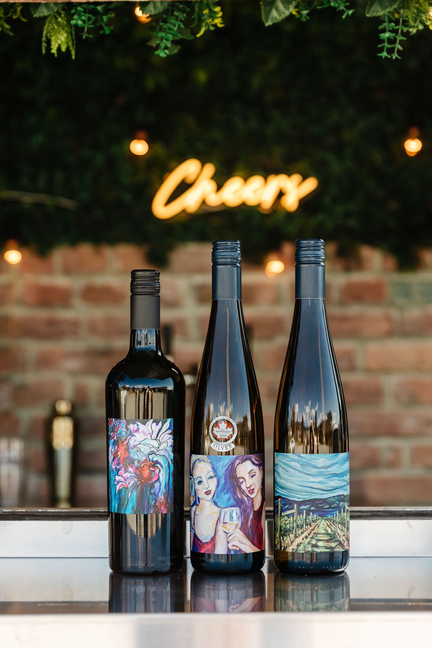 A row of dark wine bottles with colorful artistic labels displayed on a counter under warm ambient lighting.