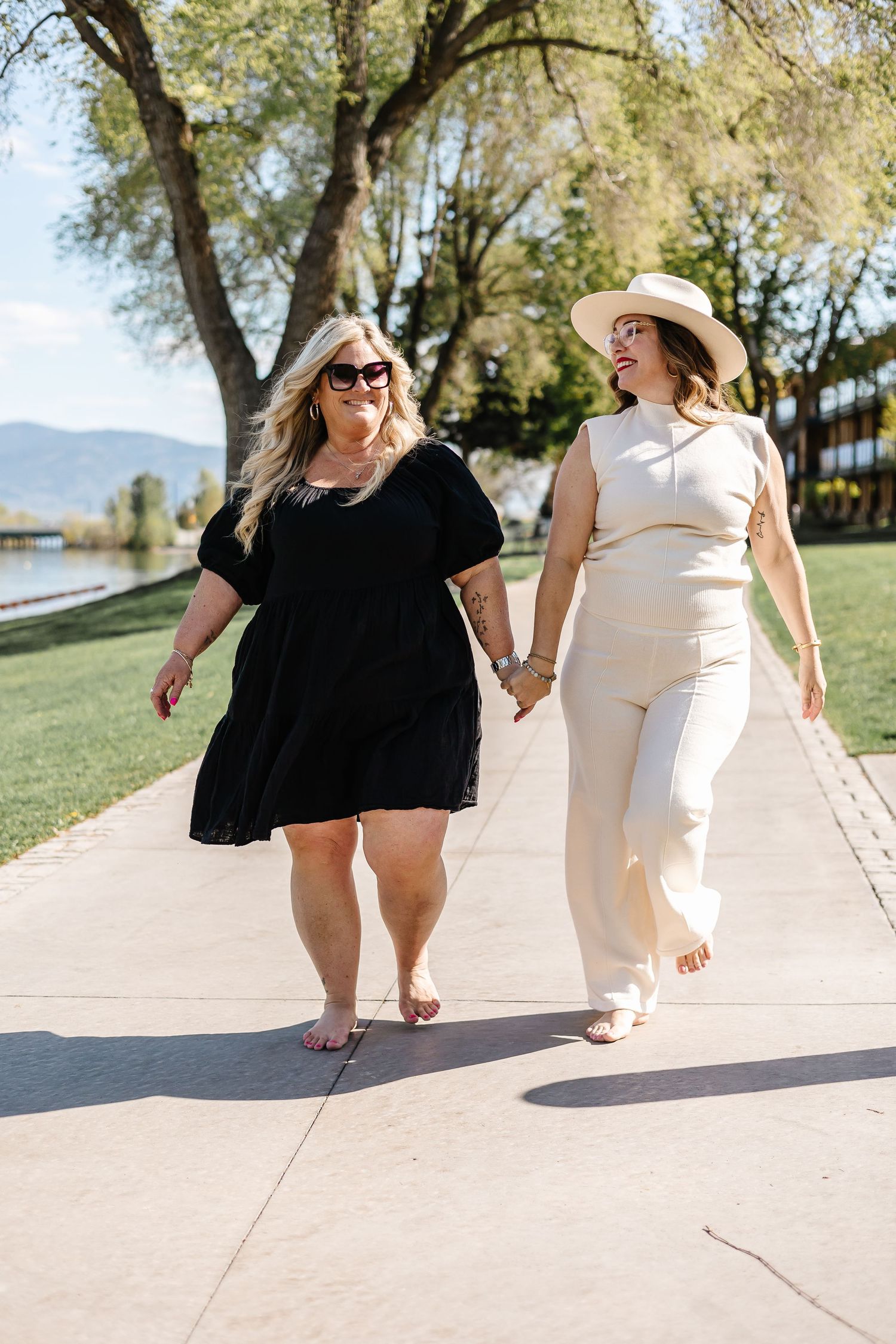 Two people walking and laughing together on a sunny path near trees.