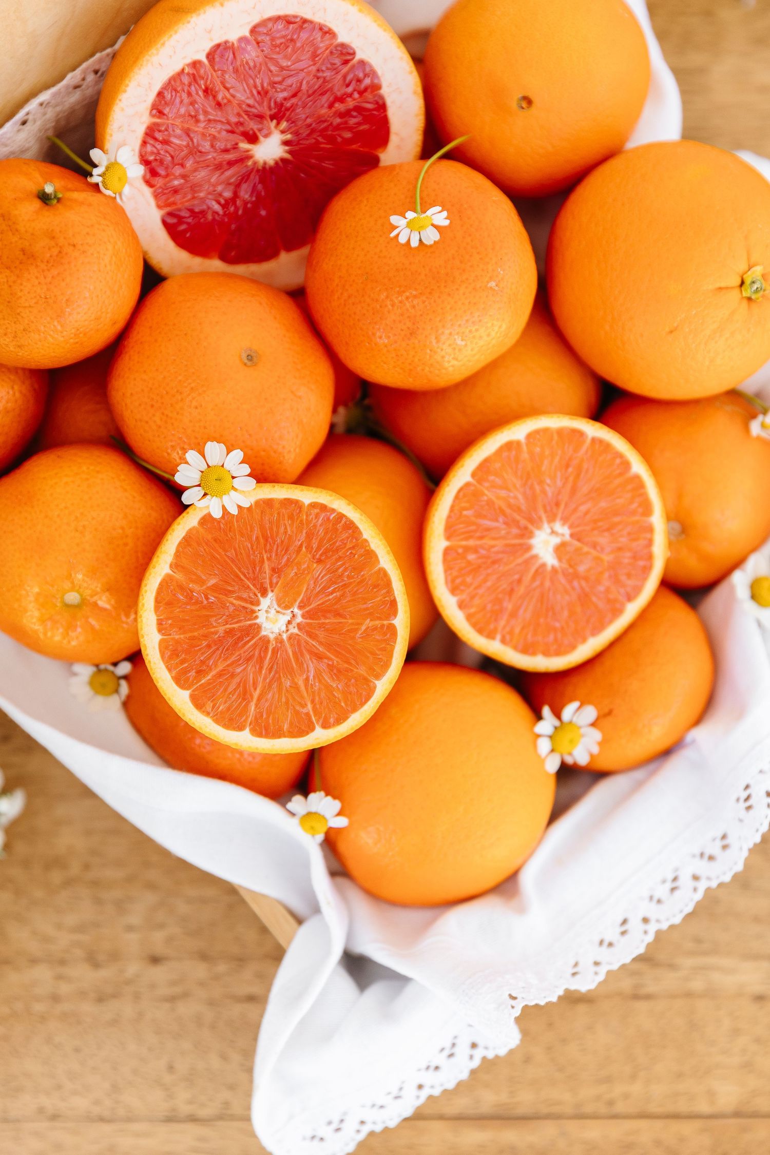 Bright oranges and grapefruits displayed with small daisies on white doily paper.