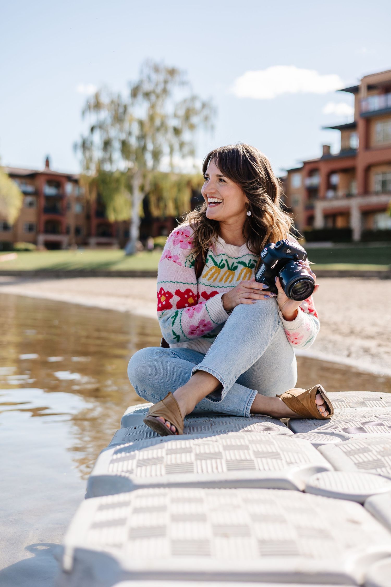 A photographer relaxes on a checkered blanket by the waterfront near apartment buildings.