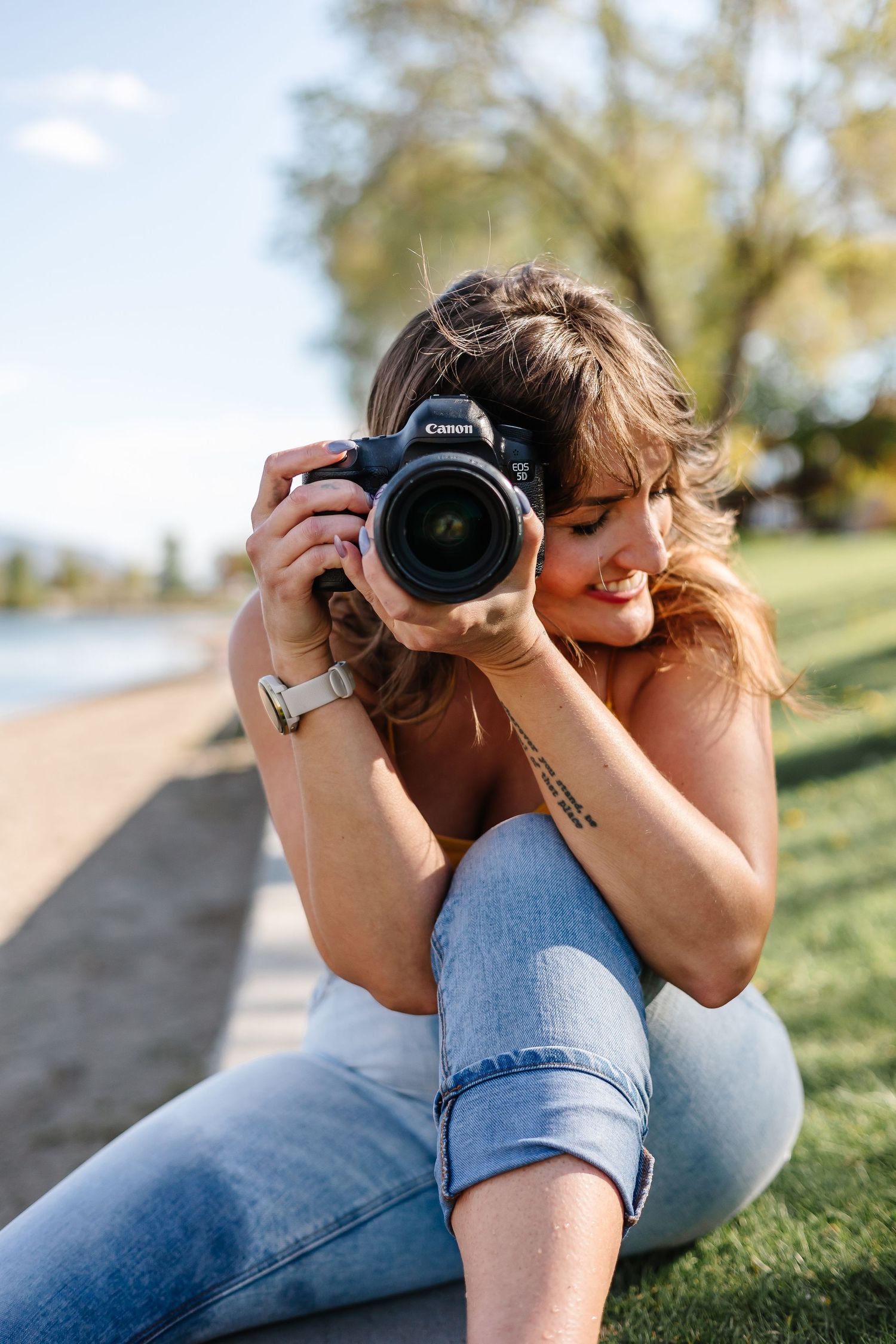 A photographer lying on grass takes photos with a Canon camera on a sunny day.