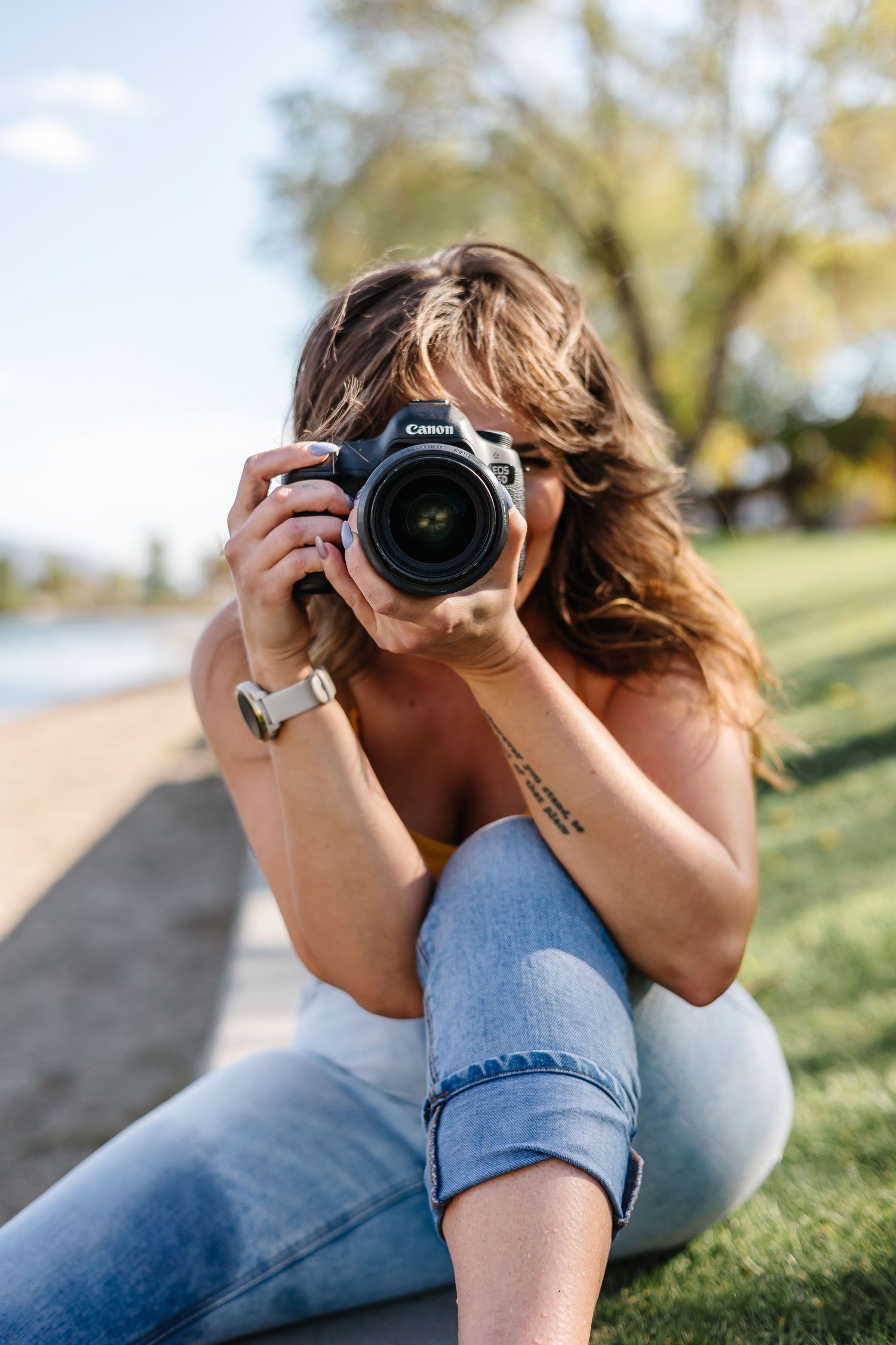 A photographer in casual attire takes photos while lying on grassy ground.