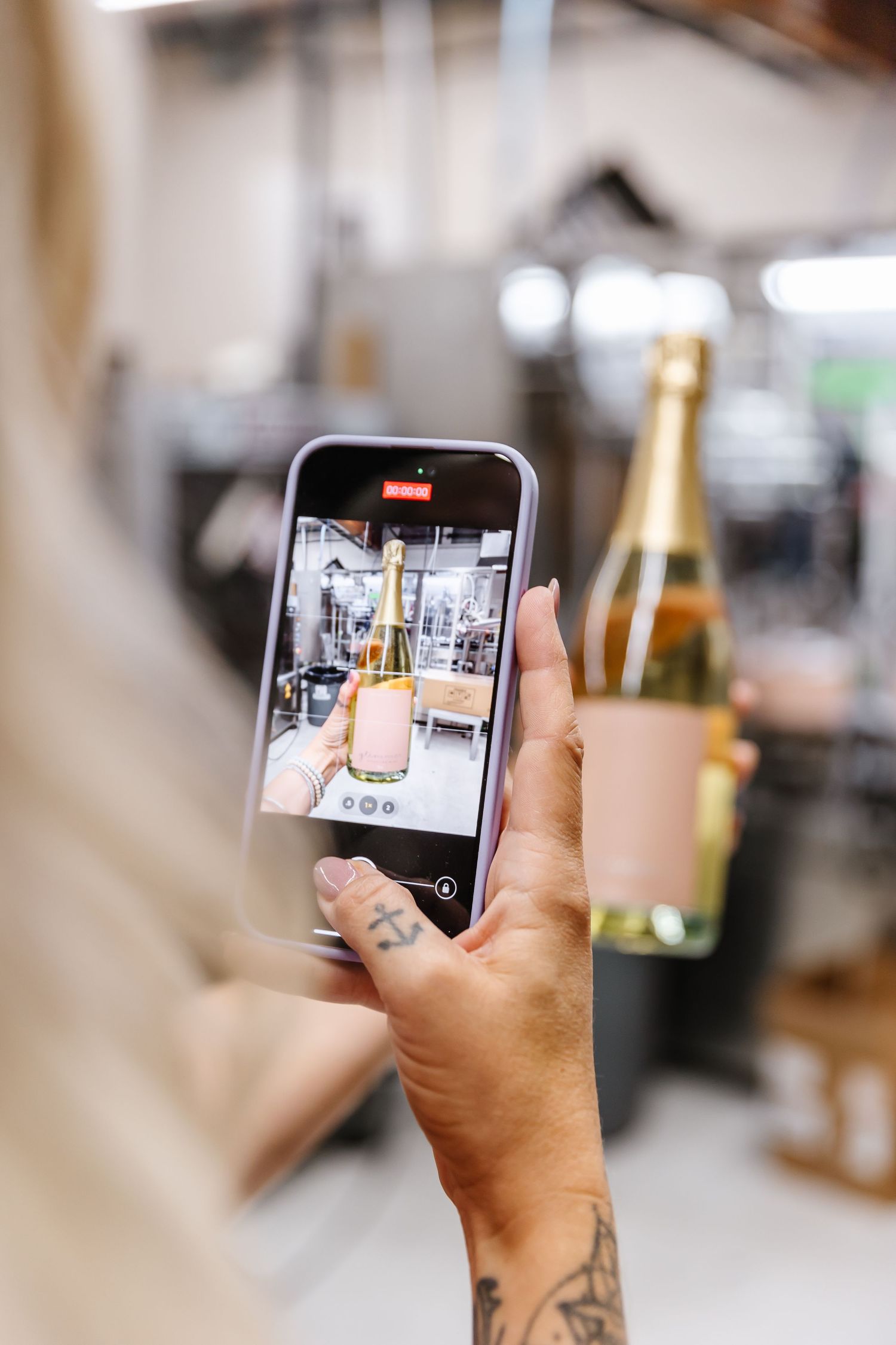 Tattooed hand holding phone taking photo of champagne bottle and glass.