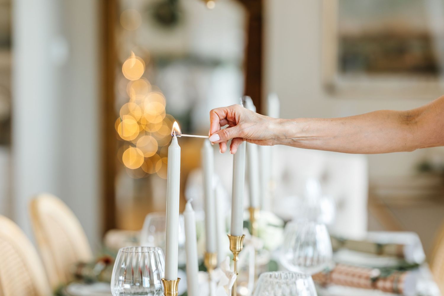 A hand pours wine into elegant glasses at an upscale dining table with soft glowing lights in the background.