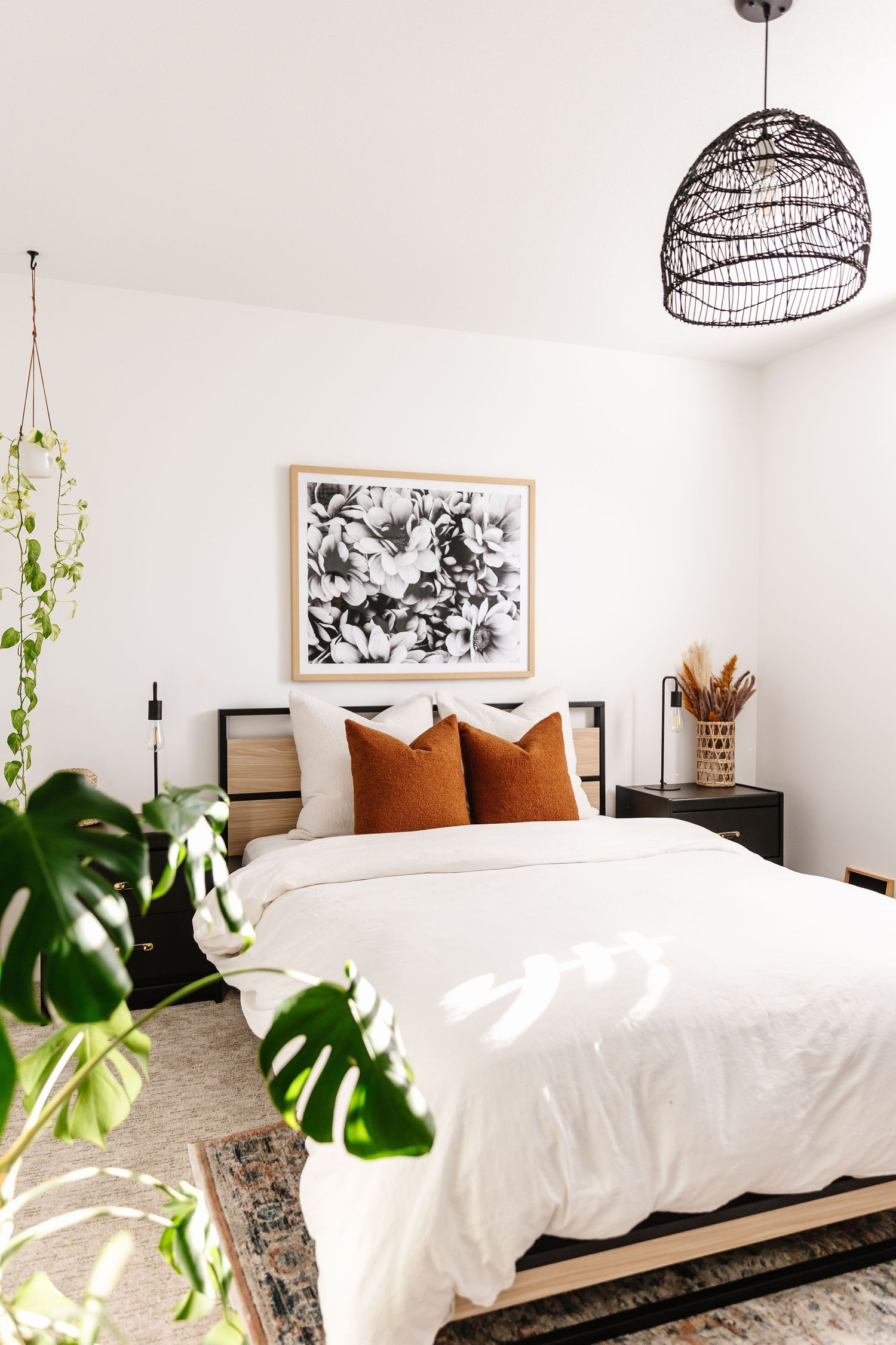 Modern bedroom with white bedding, black pendant lights, and botanical artwork.
