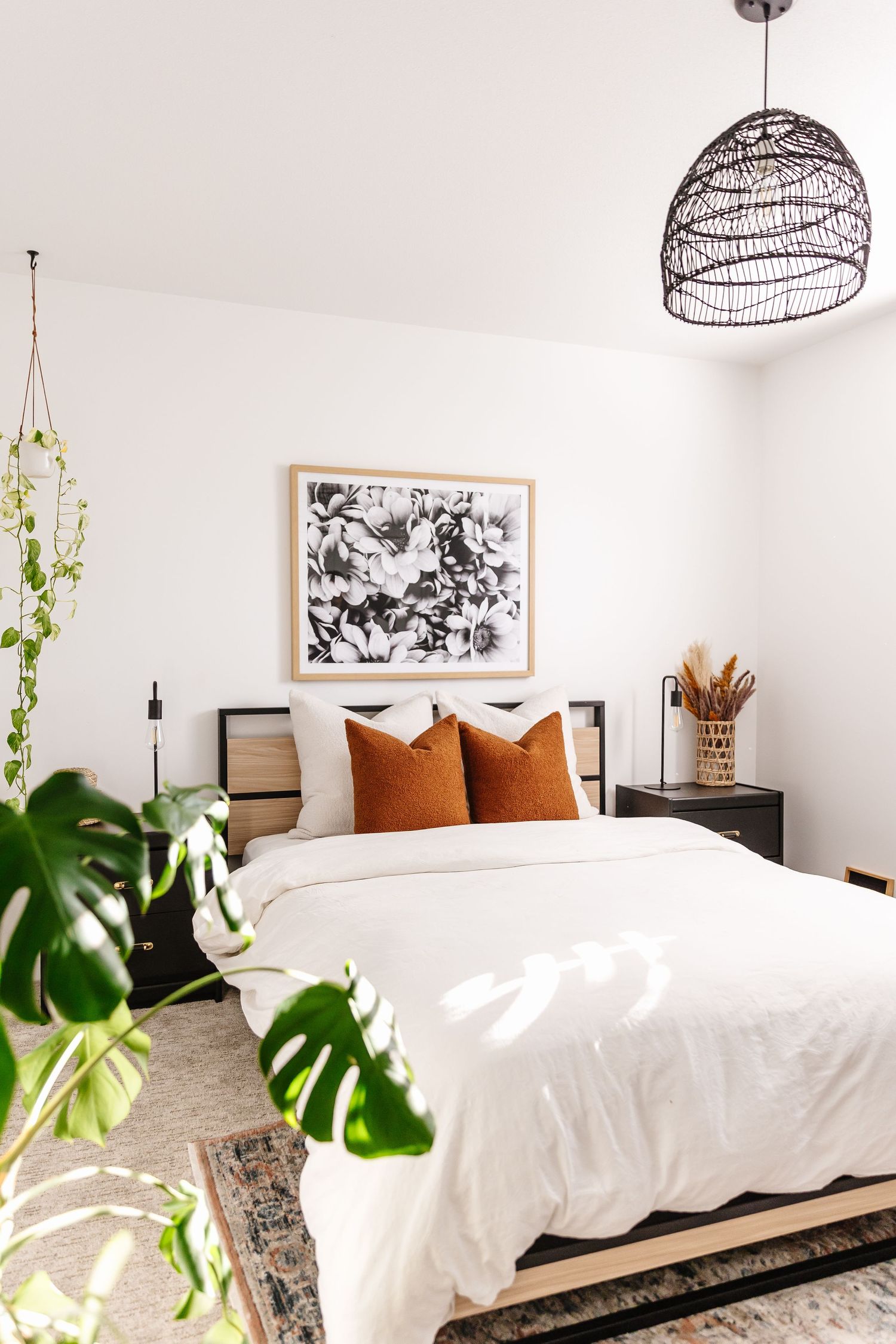 Bright bedroom featuring rattan pendant lights, white bedding and monstera plants.